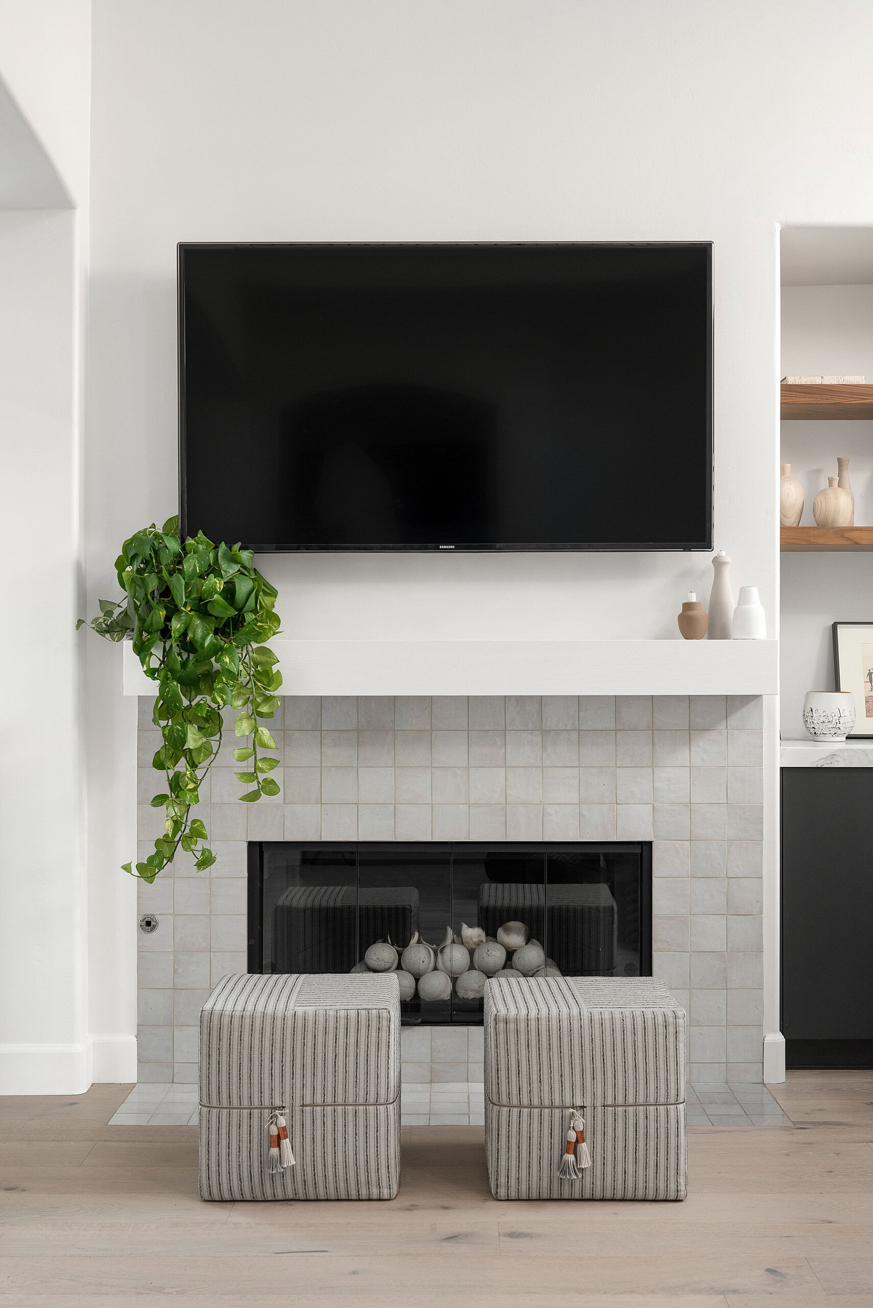 Modern living room fireplace with mounted TV and two striped ottomans.
