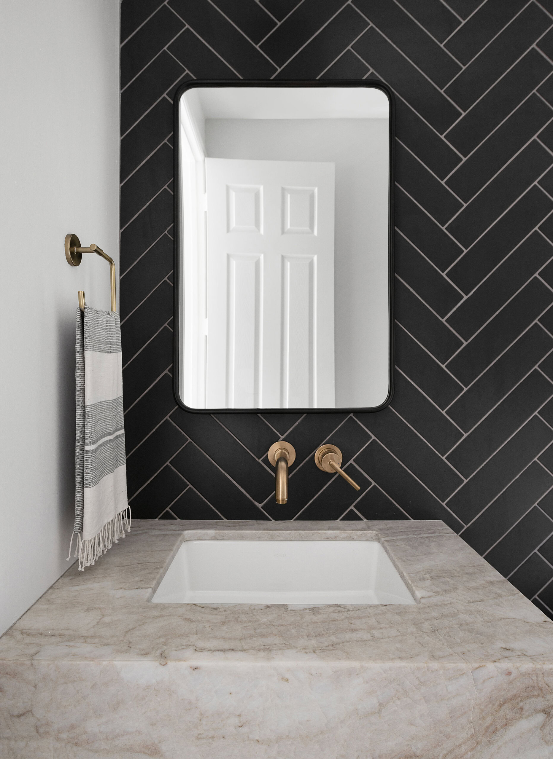 Elegant bathroom featuring black herringbone tile, a large mirror, and contemporary fixtures.