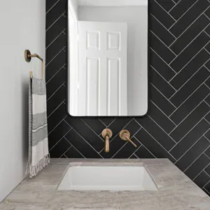 Elegant black herringbone tile wall with a white marble countertop and stylish fixtures.