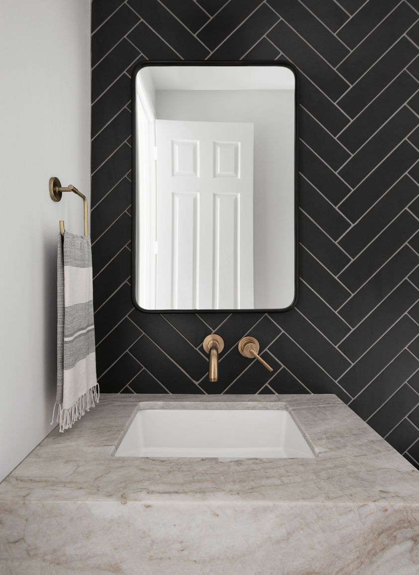 Elegant black herringbone tile wall with a white marble countertop and stylish fixtures.