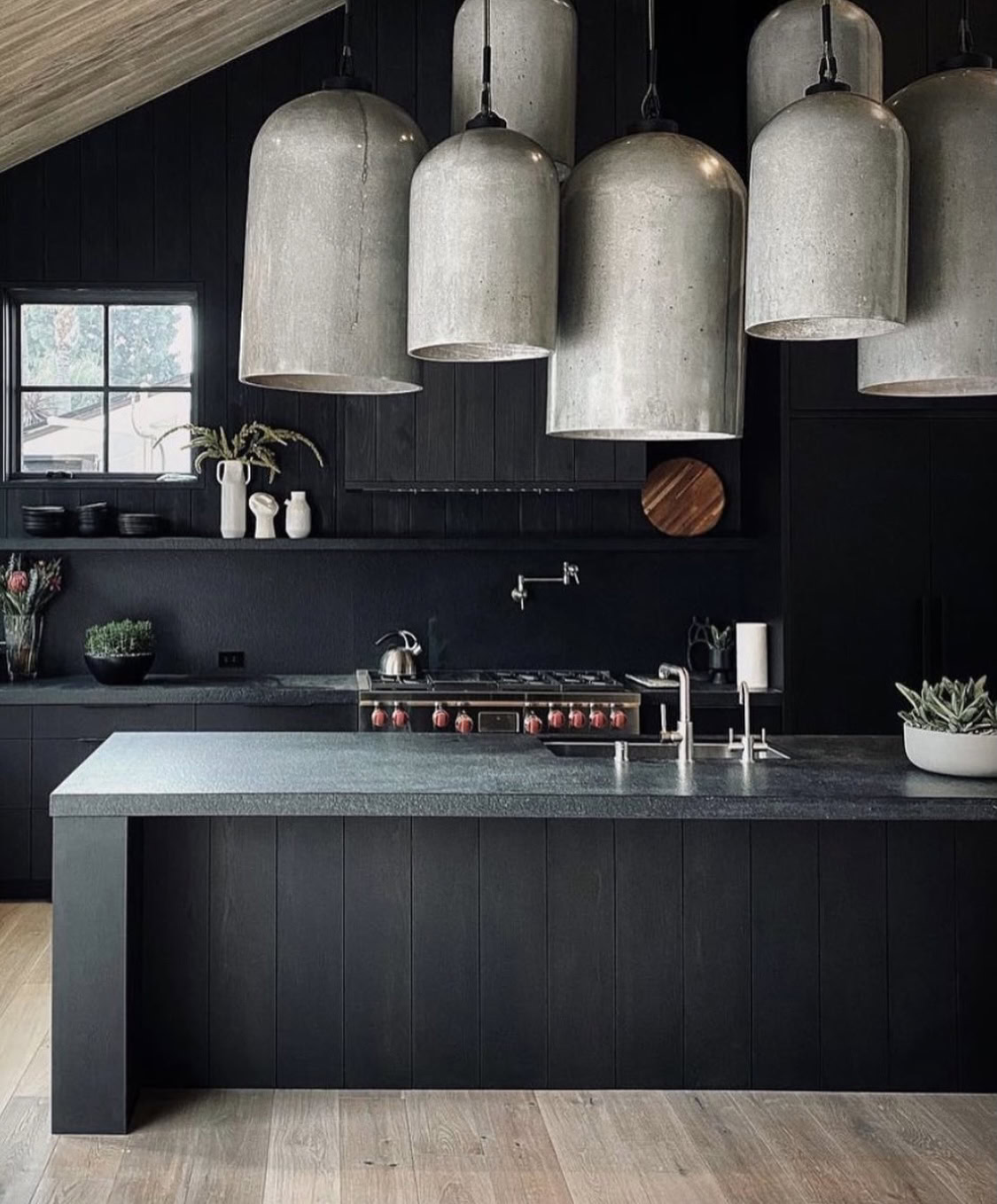 Black kitchen with large concrete pendant lights and sleek countertops.