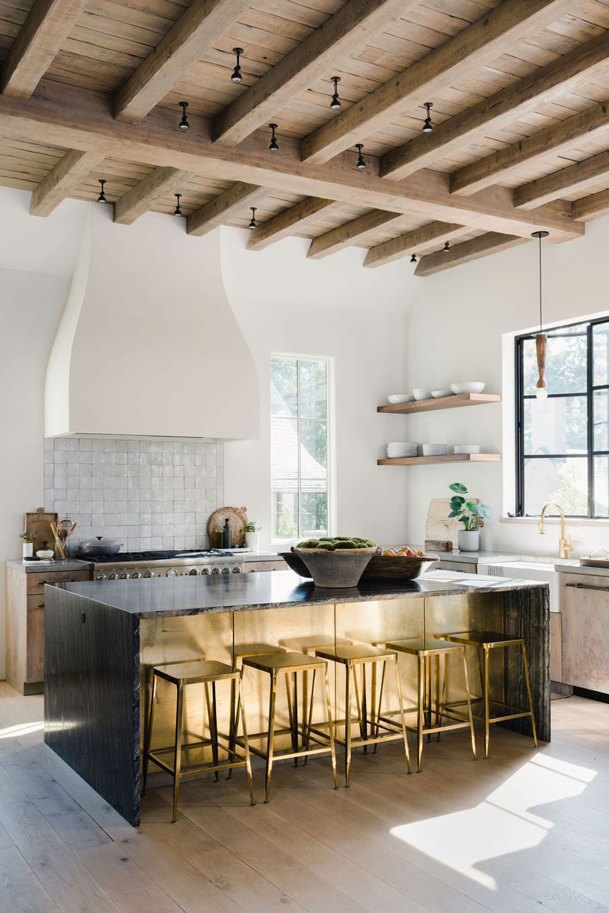 Modern rustic kitchen featuring wooden beamed ceiling and sleek black island with gold stools.