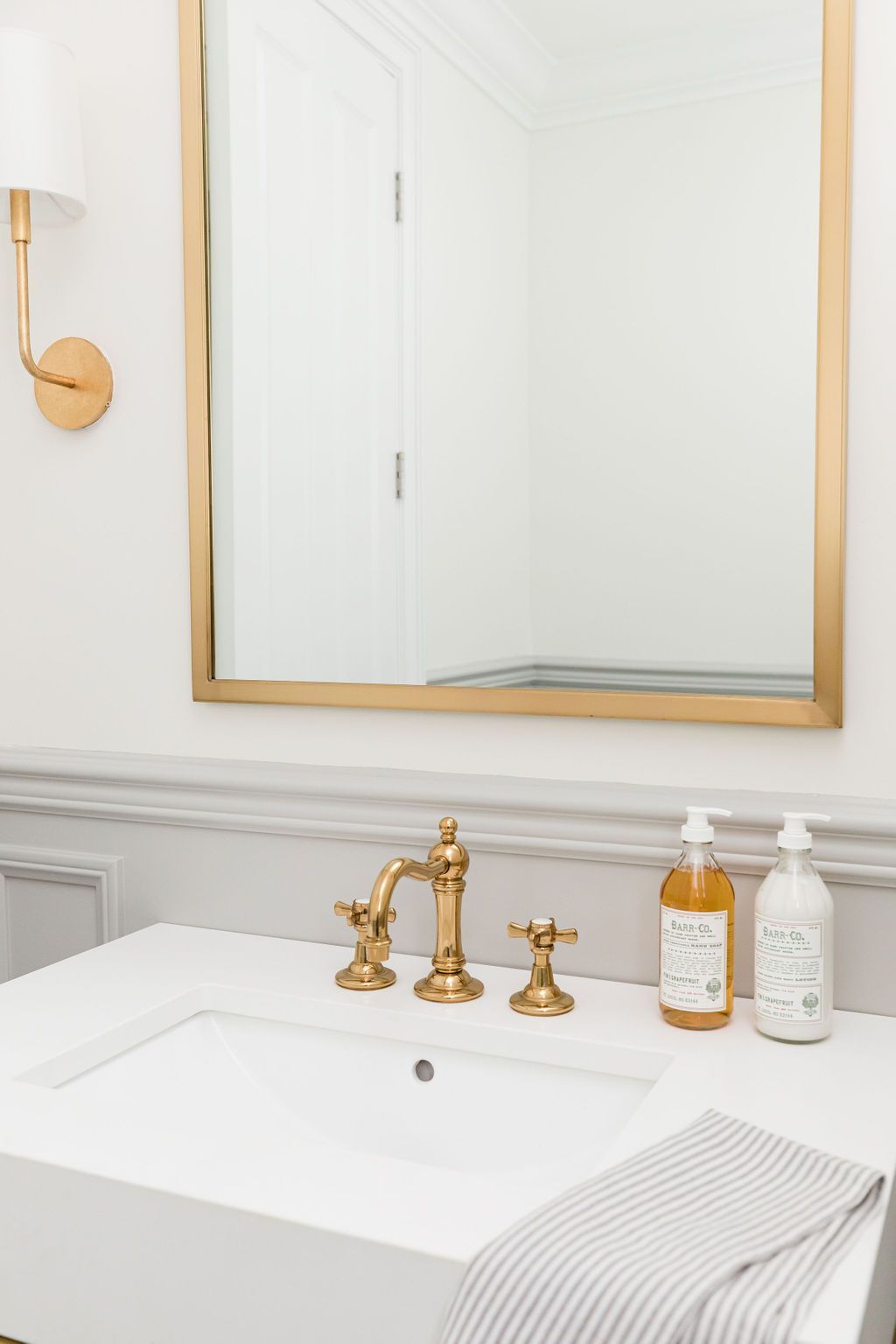 Elegant gold faucet with white bathroom vanity and mirror, modern interior design.