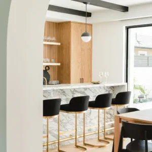Contemporary kitchen featuring marble island and stylish black bar stools with gold accents. Bright,.