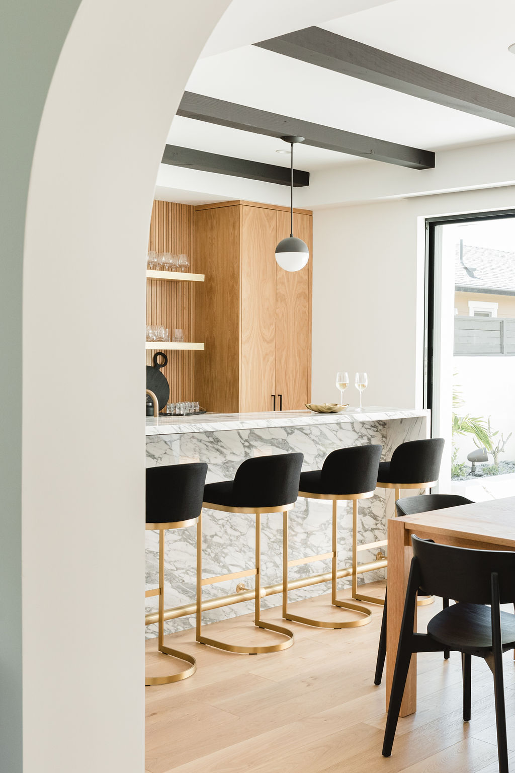 Contemporary kitchen featuring marble island and stylish black bar stools with gold accents. Bright,.