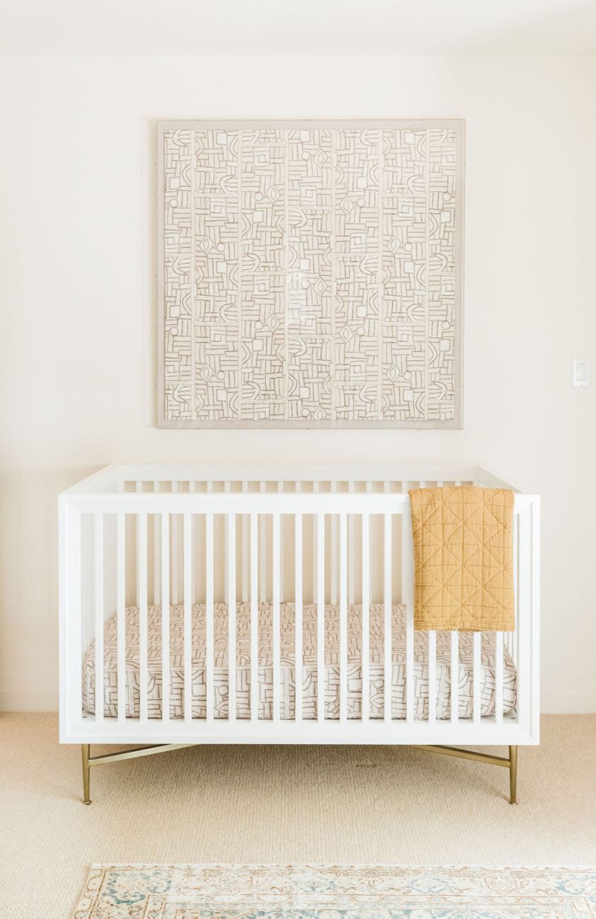 Baby crib with white slats in a nursery with geometric wall decor.