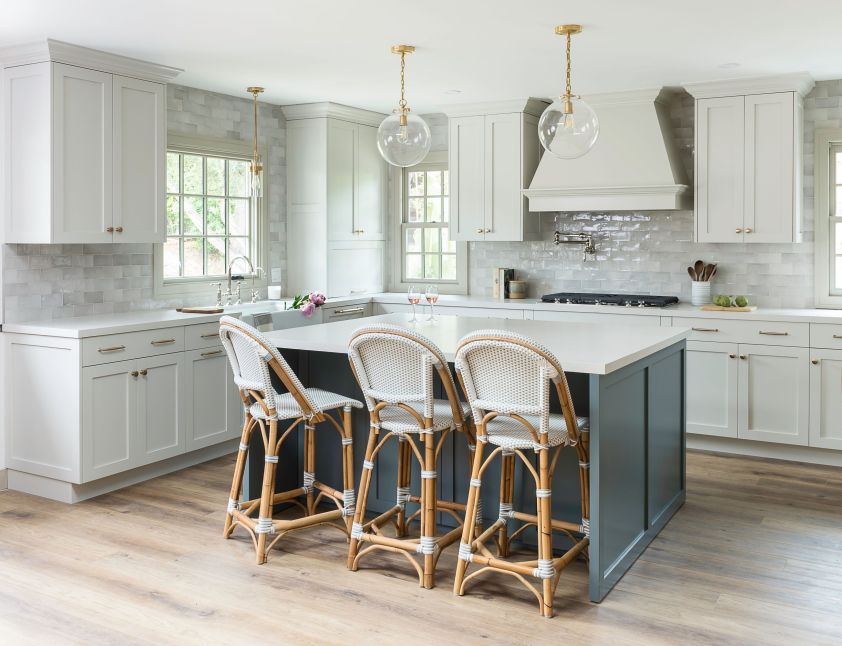 Bright white kitchen featuring a stylish blue island, elegant pendant lighting, and ample natural su.