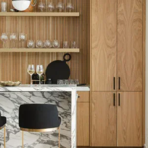 Stylish wooden kitchen with marble countertop, open shelves, and glassware display.