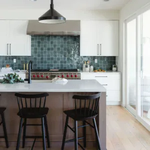 Bright modern kitchen featuring white cabinets, a blue tile backsplash, and black bar stools.