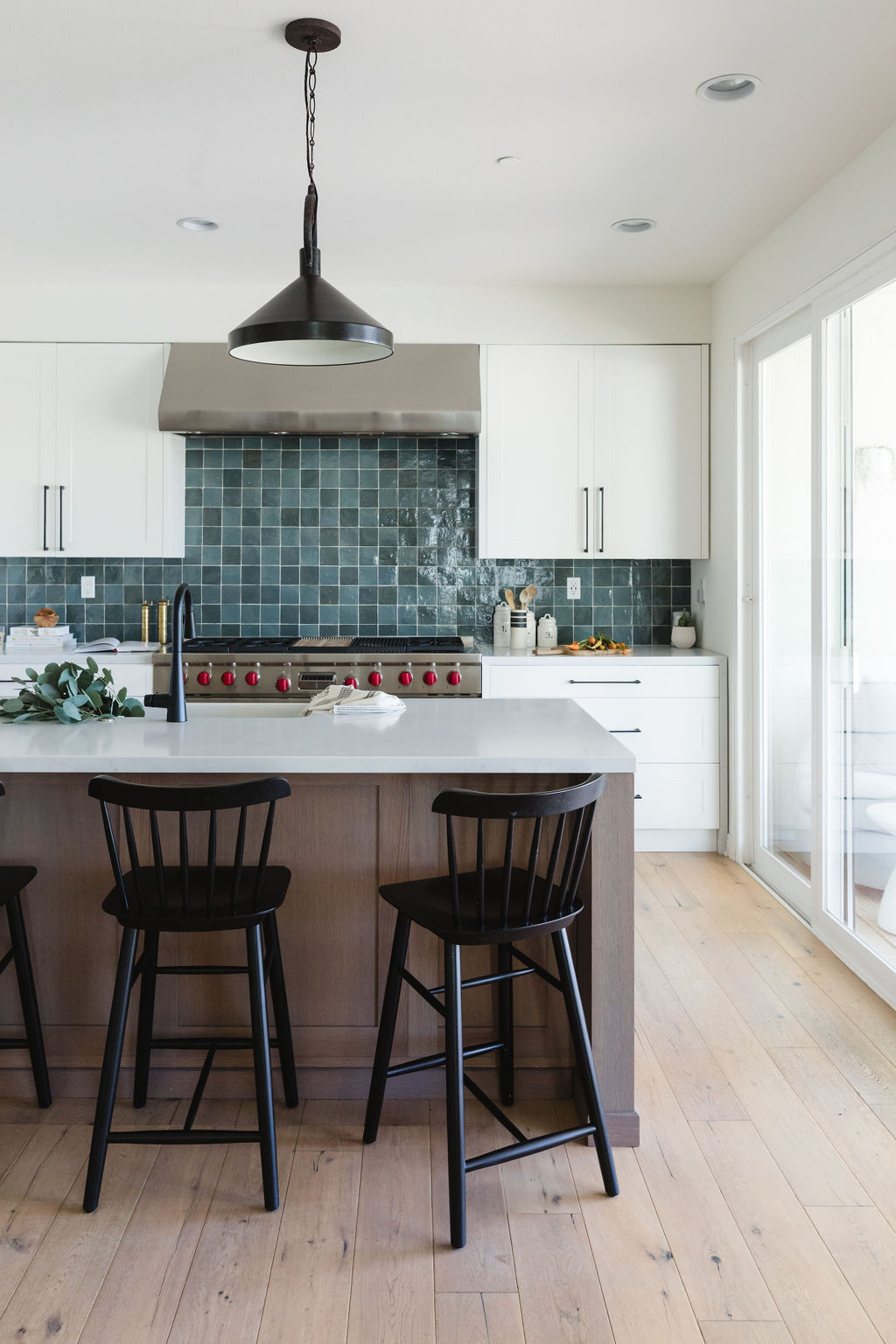 Bright modern kitchen featuring white cabinets, a blue tile backsplash, and black bar stools.