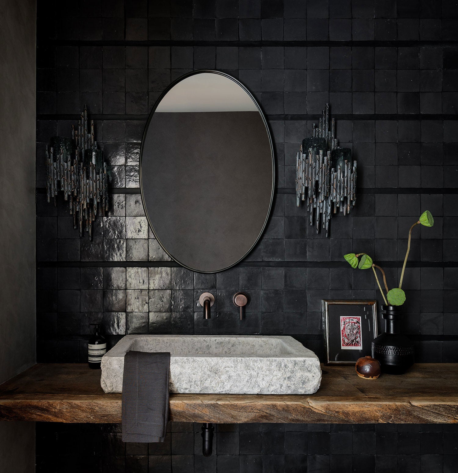 Stylish black tiled bathroom featuring a marble sink, mirror, and contemporary lighting fixtures.
