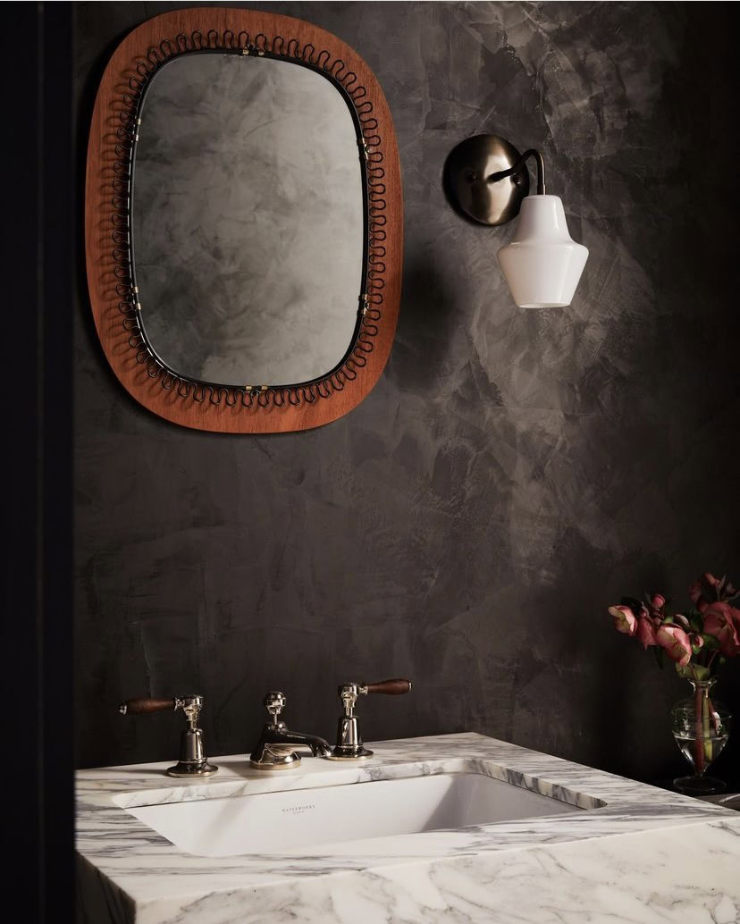 Modern interior with dark painted walls, decorative mirror, and wall-mounted light fixture.