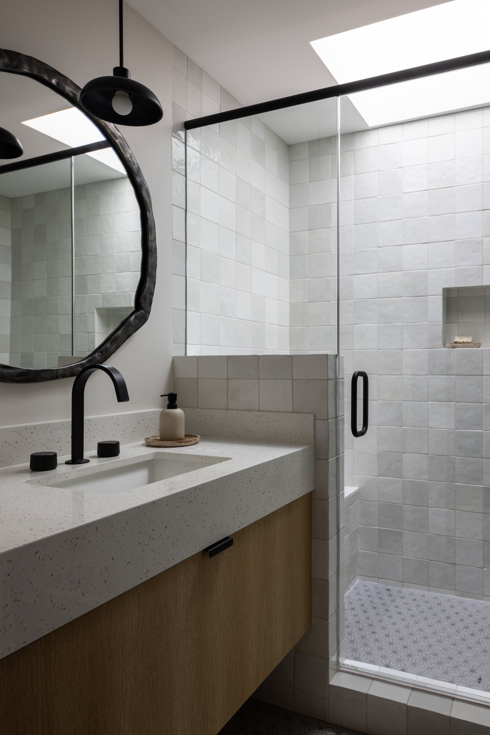 Contemporary bathroom featuring a minimalist vanity, round mirror, and walk-in shower with glass enc.