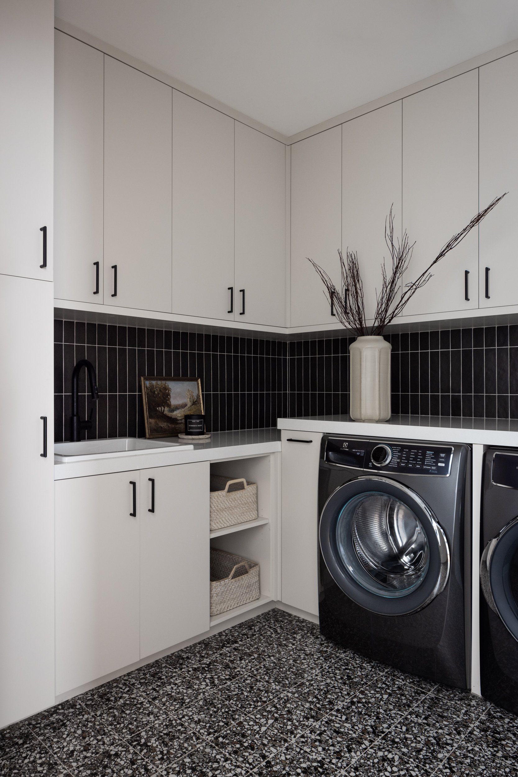 Laundry room with sleek white cabinetry and black backsplash, featuring a front-loading washer and d.