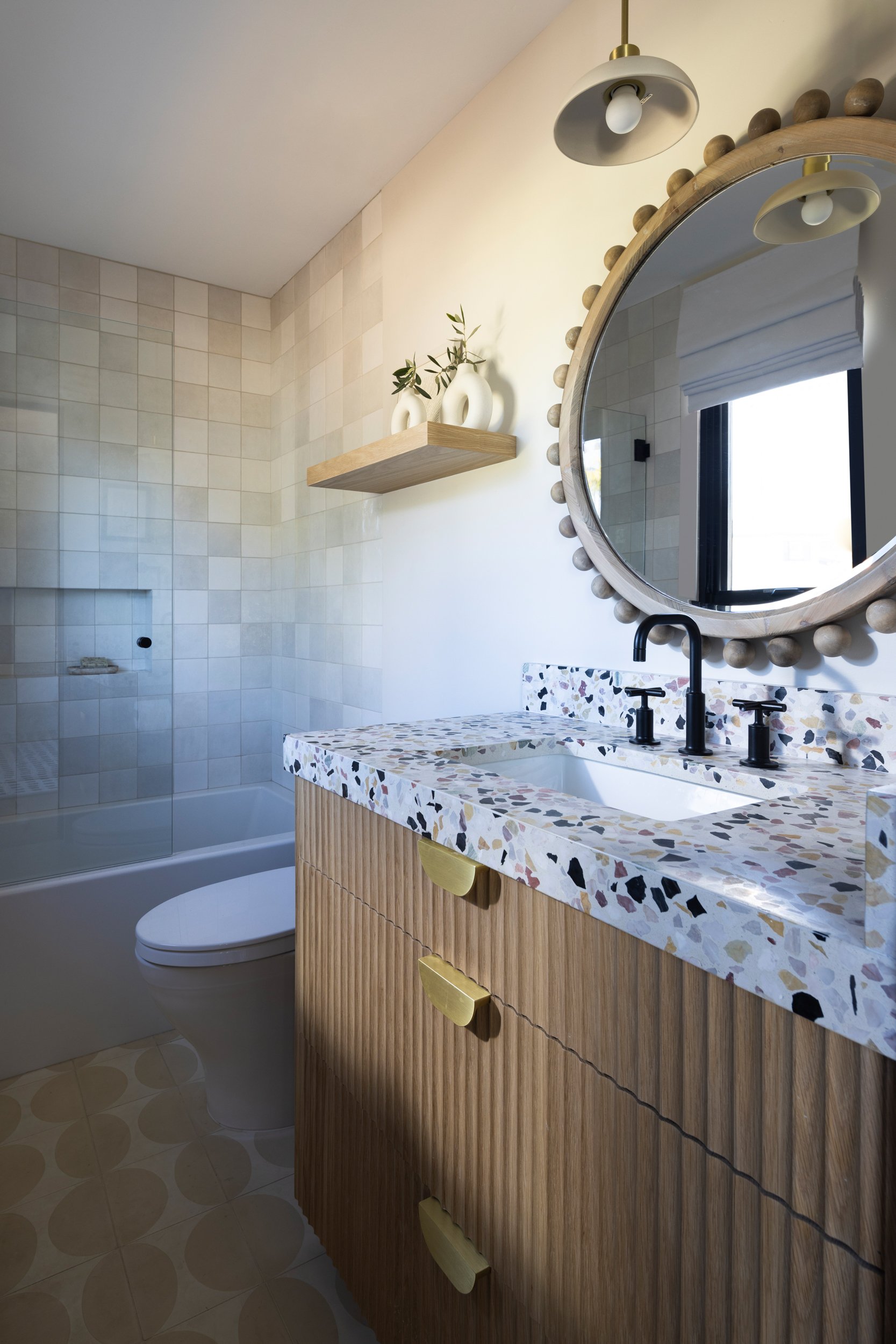 Bathroom interior with terrazzo vanity, round mirror, and minimalist decor.