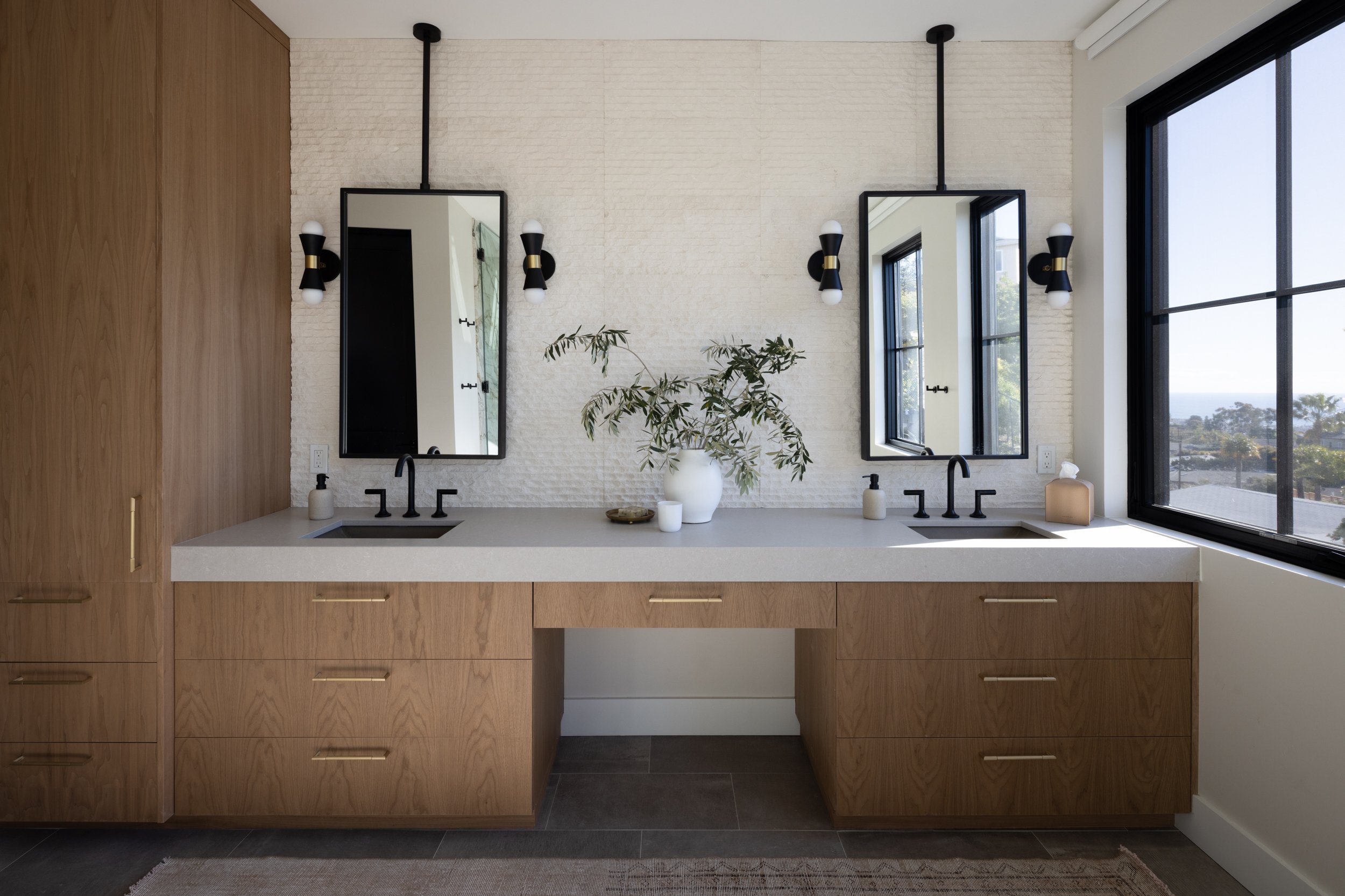Elegant bathroom with double sinks, black fixtures, and natural light from large window.