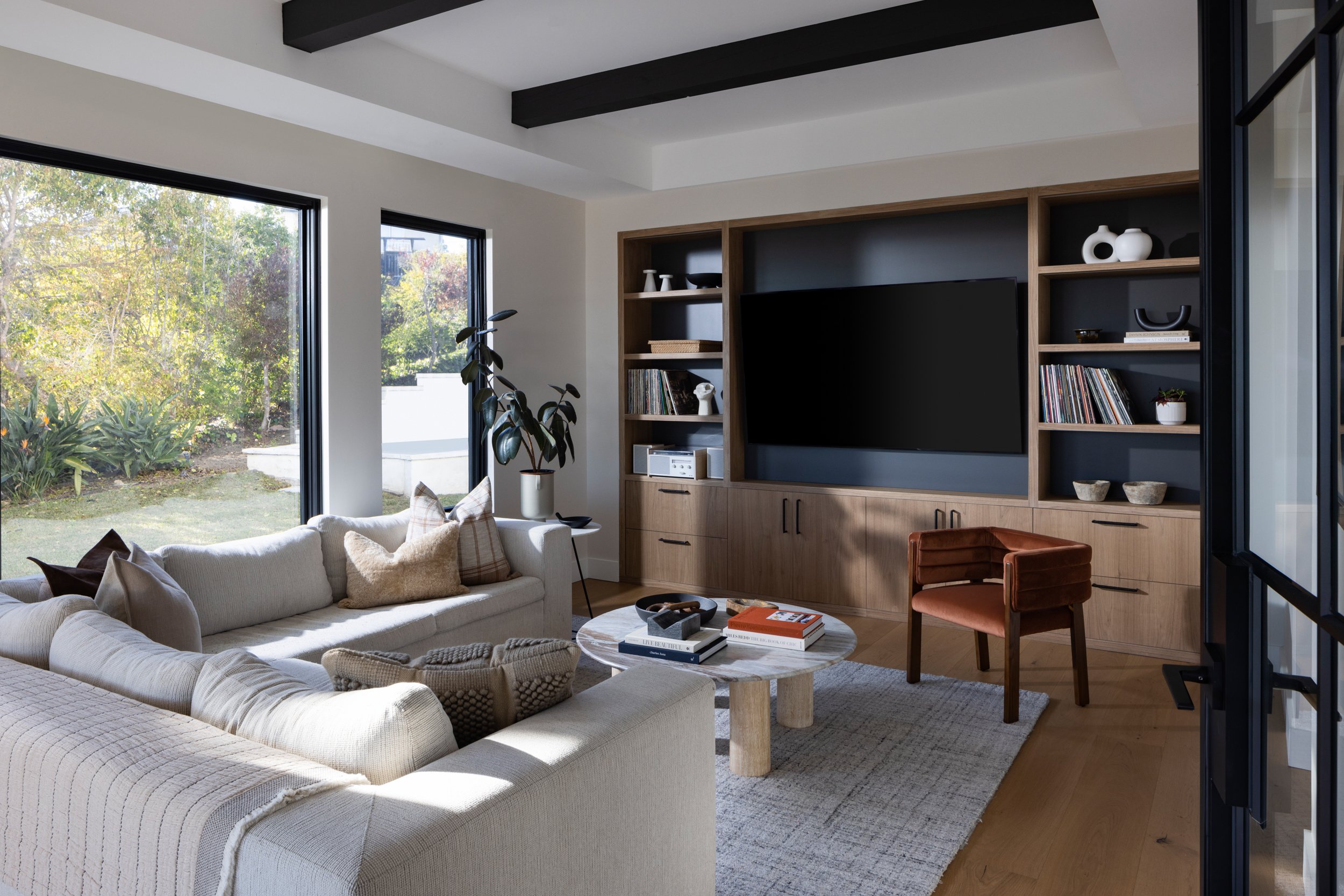 Modern living room with built-in TV unit, cozy sofa, and natural light from large windows.