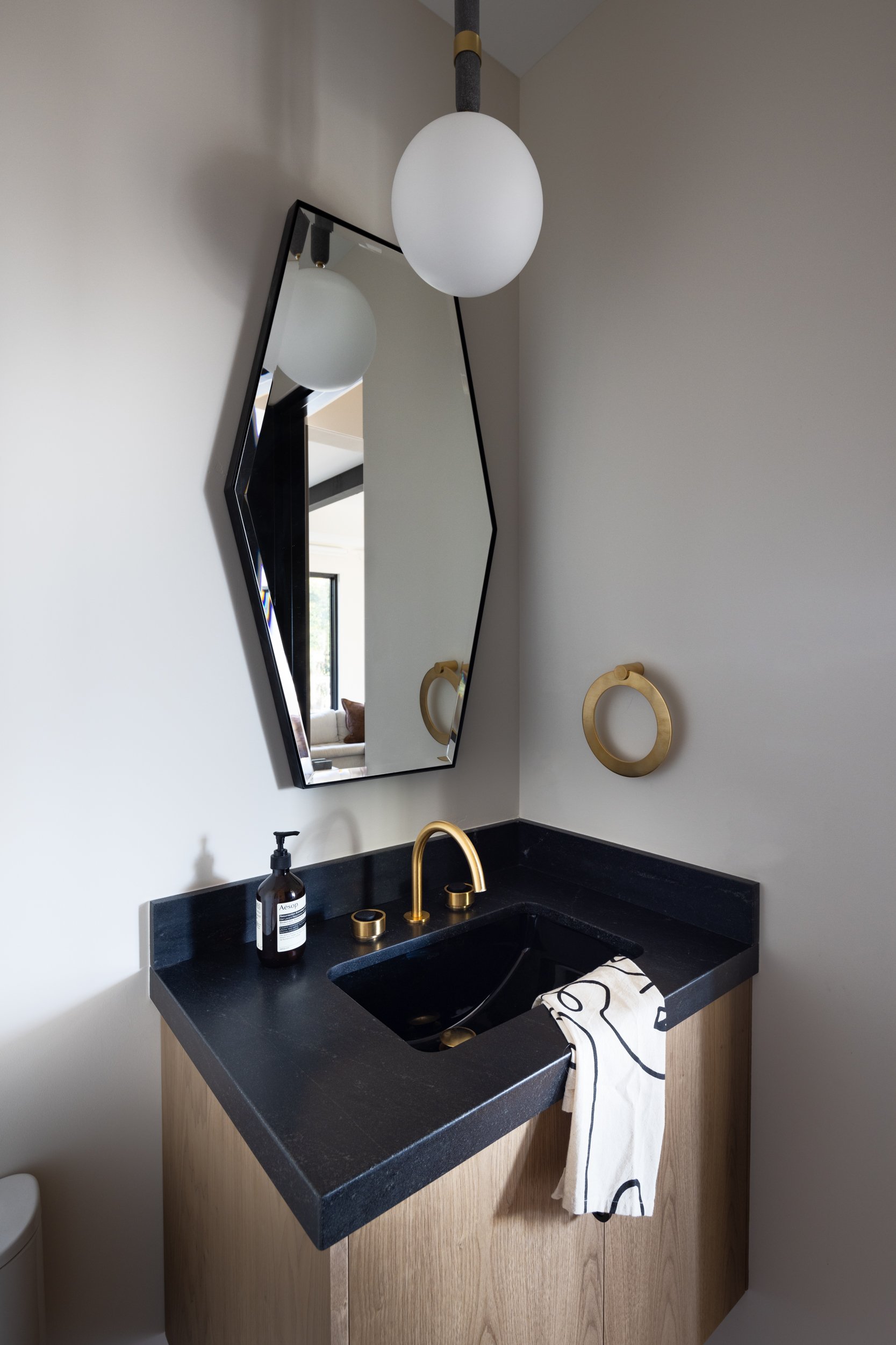 Bathroom vanity with black countertop, gold faucet, and stylish mirror.