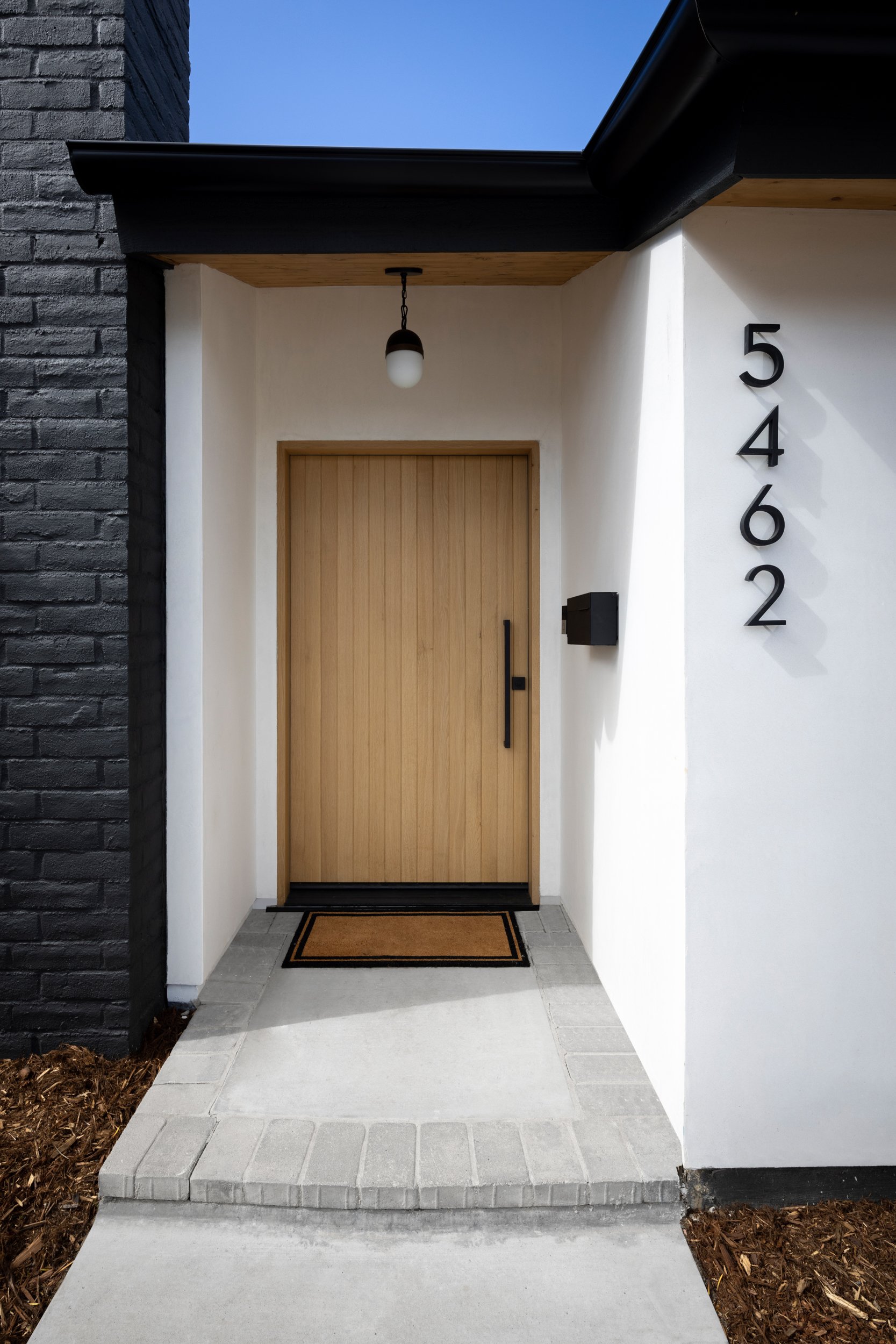 Modern front door with natural wood finish and black hardware, located at 5462 Thunderbird.