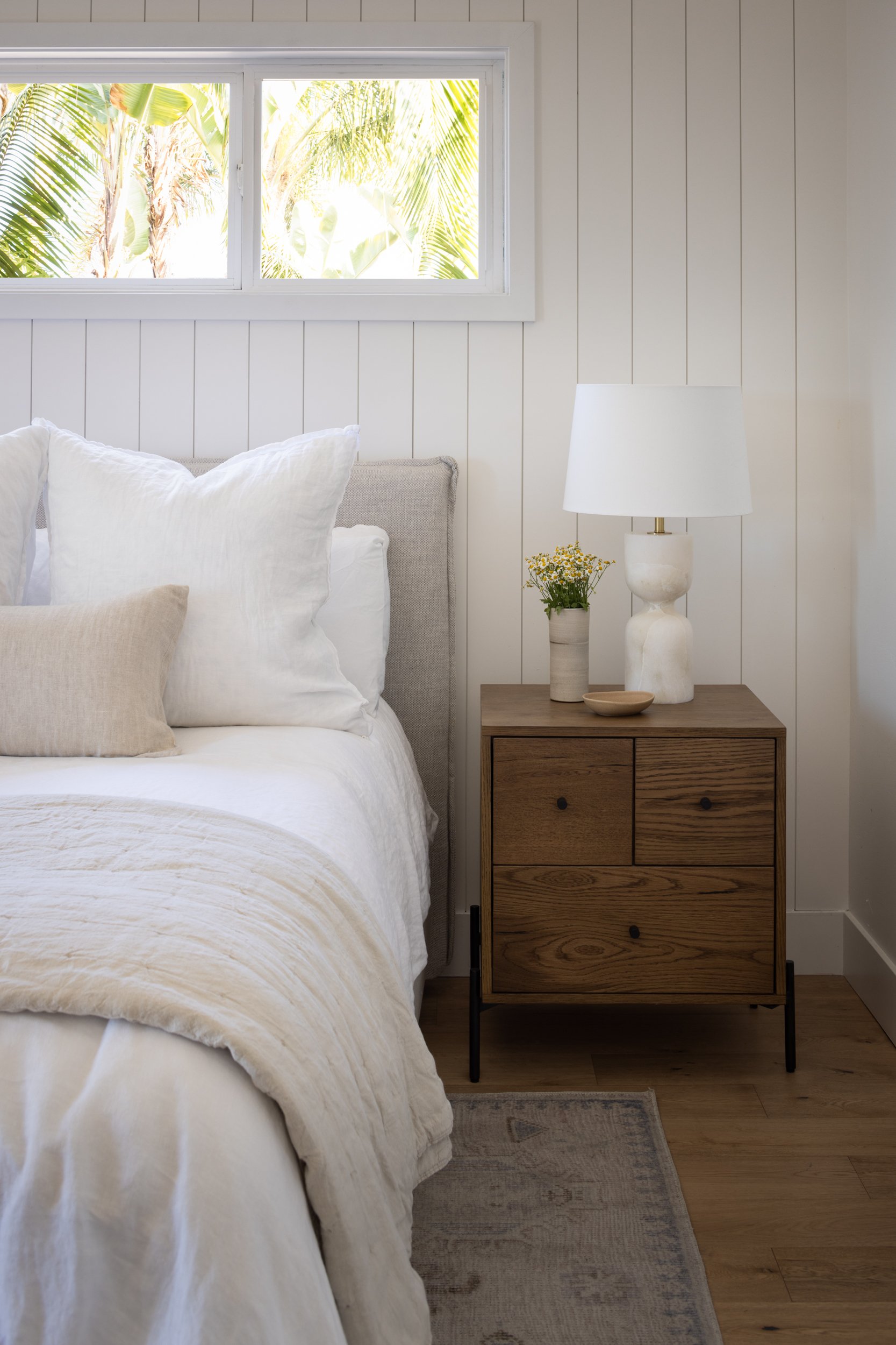 Cozy Hermosa bedroom featuring white bedding, a wooden nightstand, and natural light from a window.