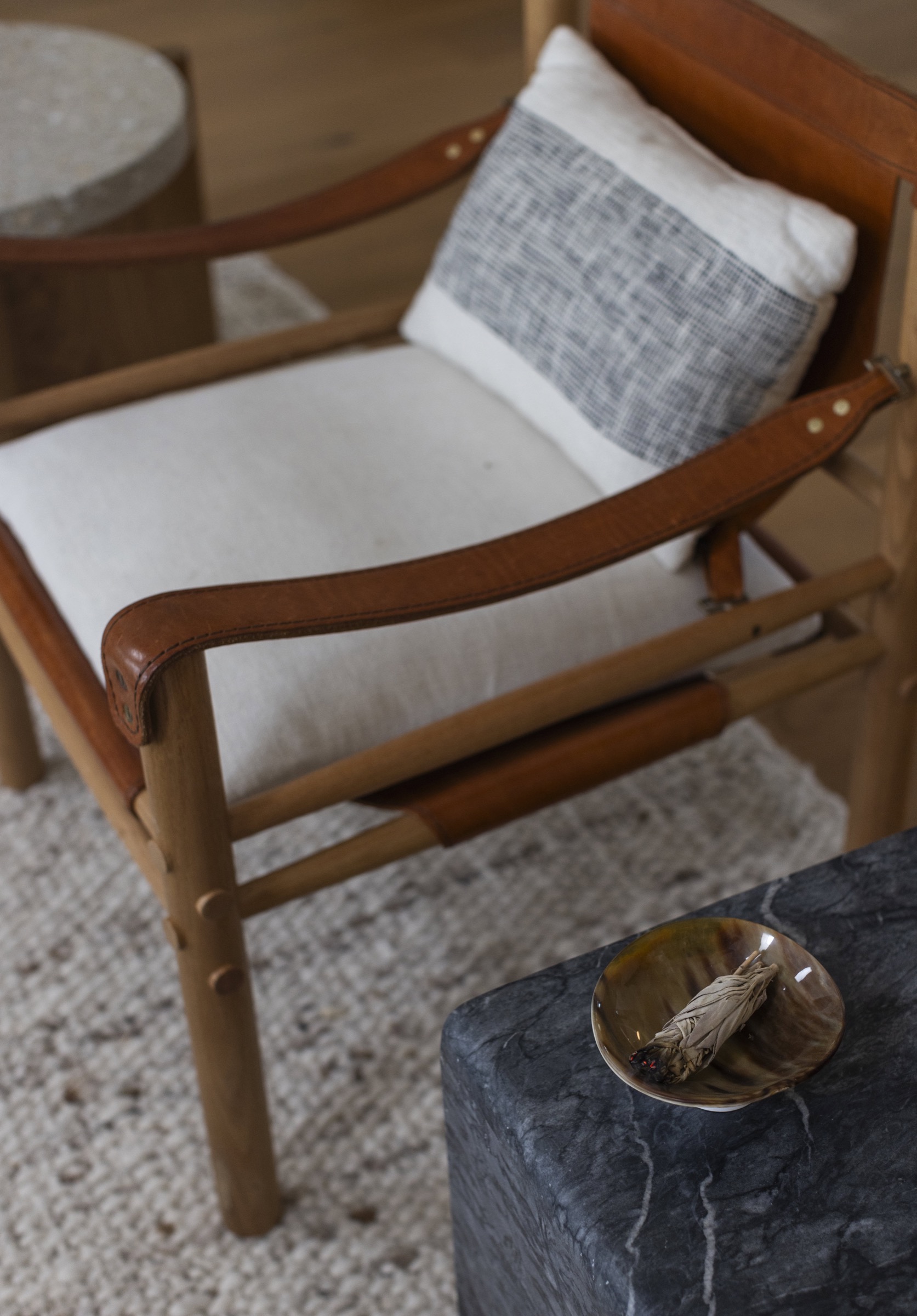 Modern wooden armchair with beige cushion and decorative pillow in interior setting.