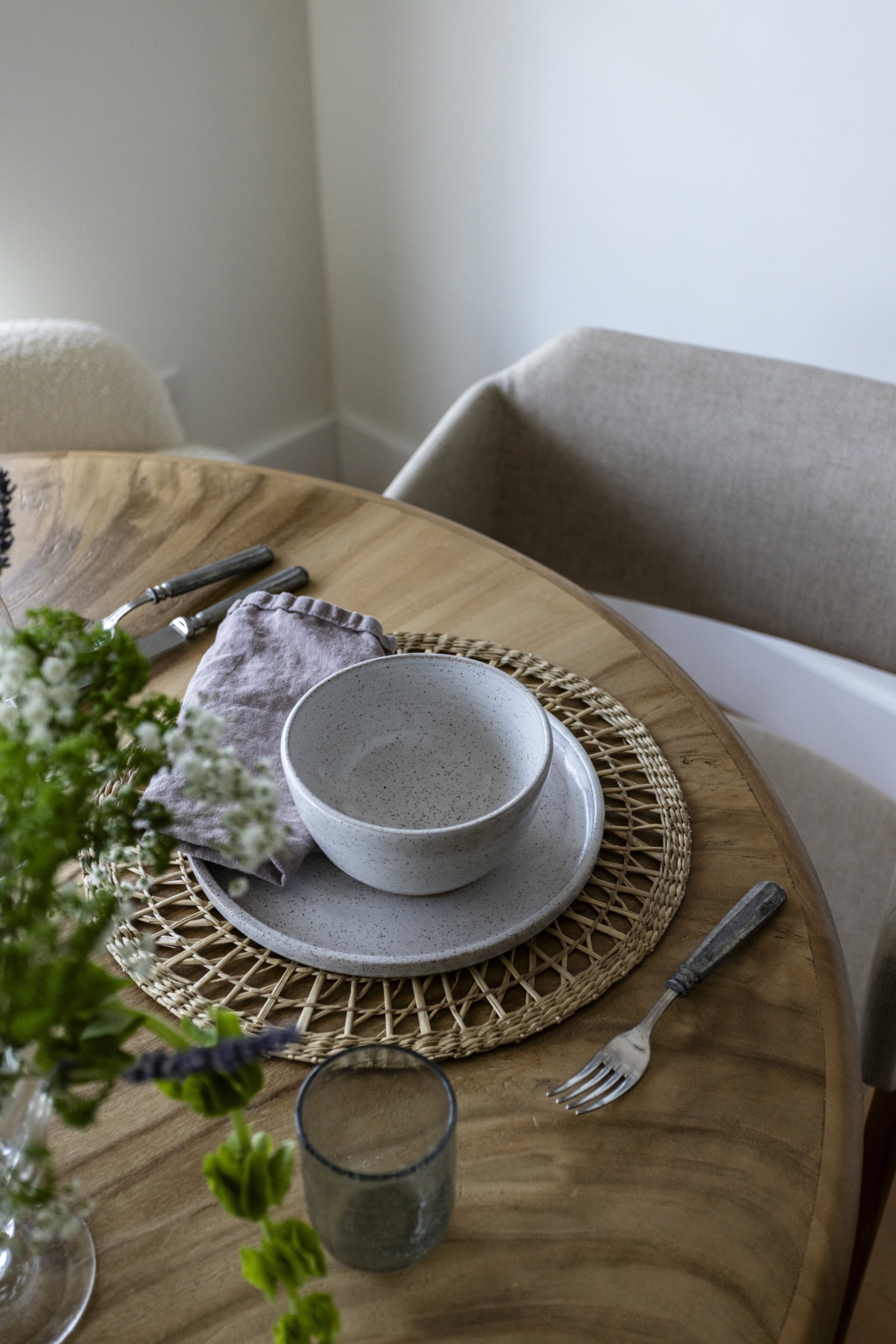 Elegant dining table with ceramic dishware and woven placemat in a bright, minimalist space.