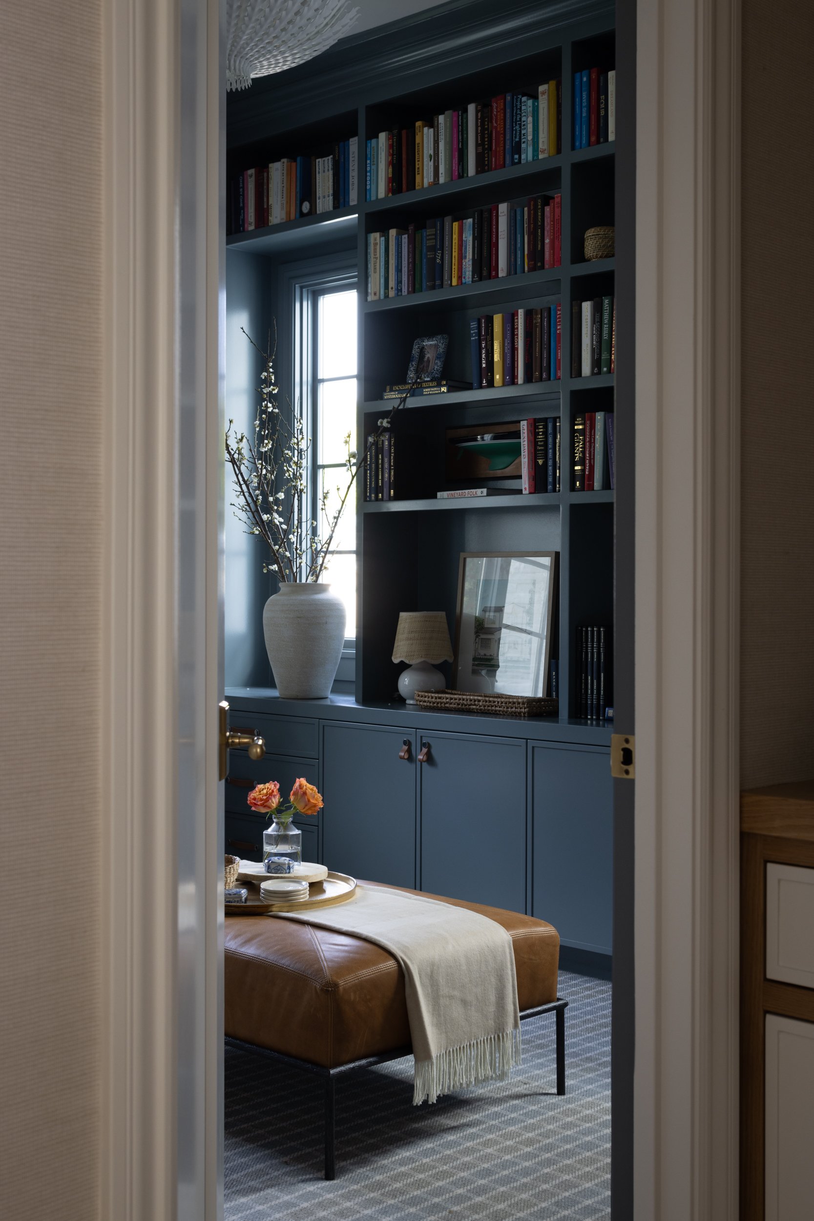 Elegant built-in blue bookshelves with a window, filled with colorful books and decorative items.