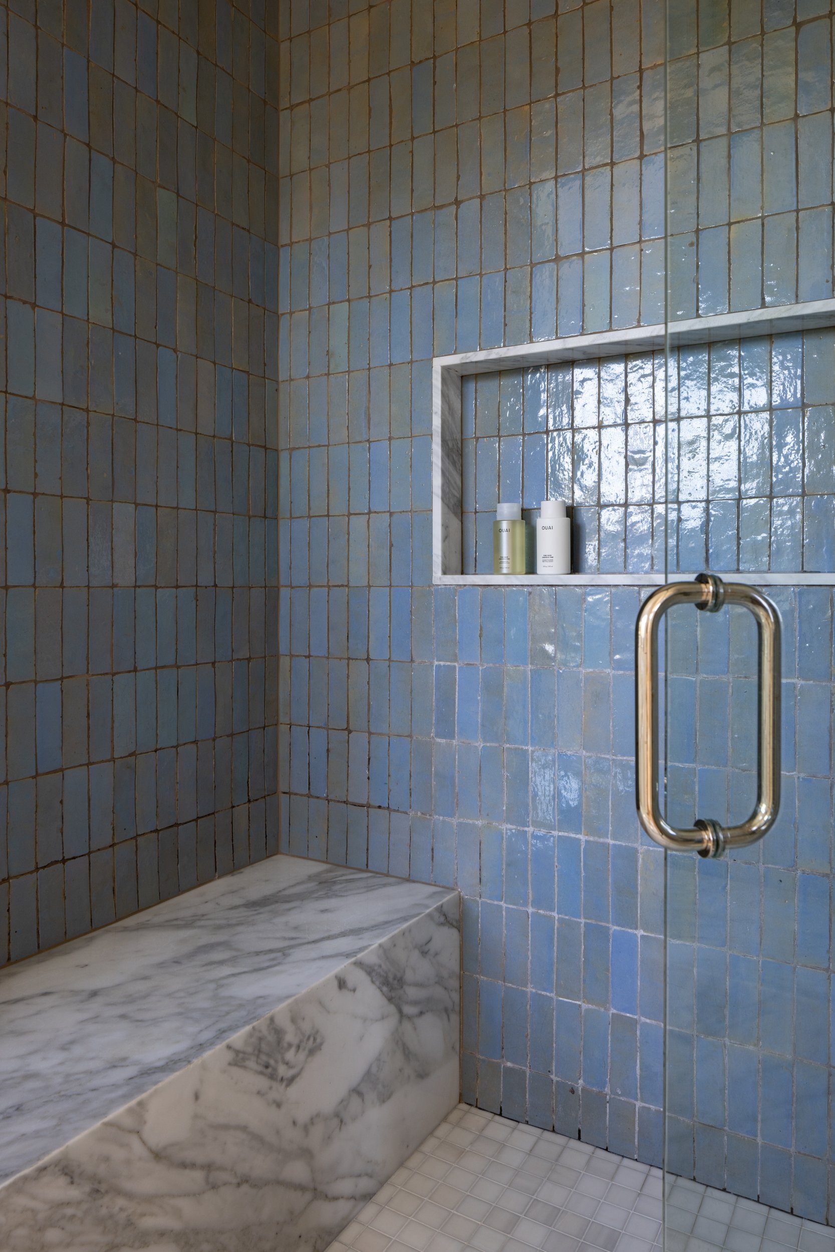Blue tiled shower with marble bench and built-in niche.