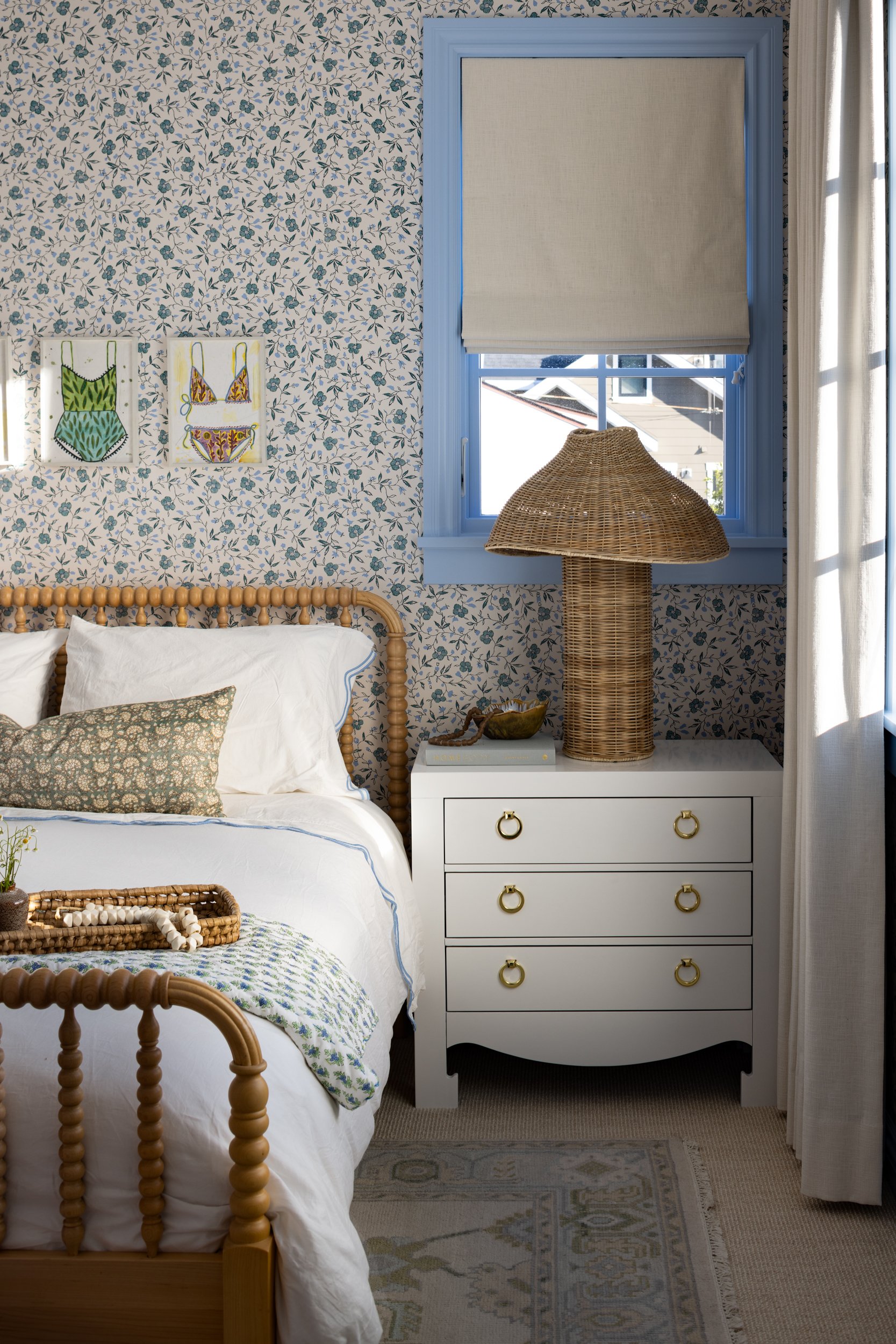 Charming coastal bedroom with floral wallpaper and wicker furniture accents. Bright, airy space feat.