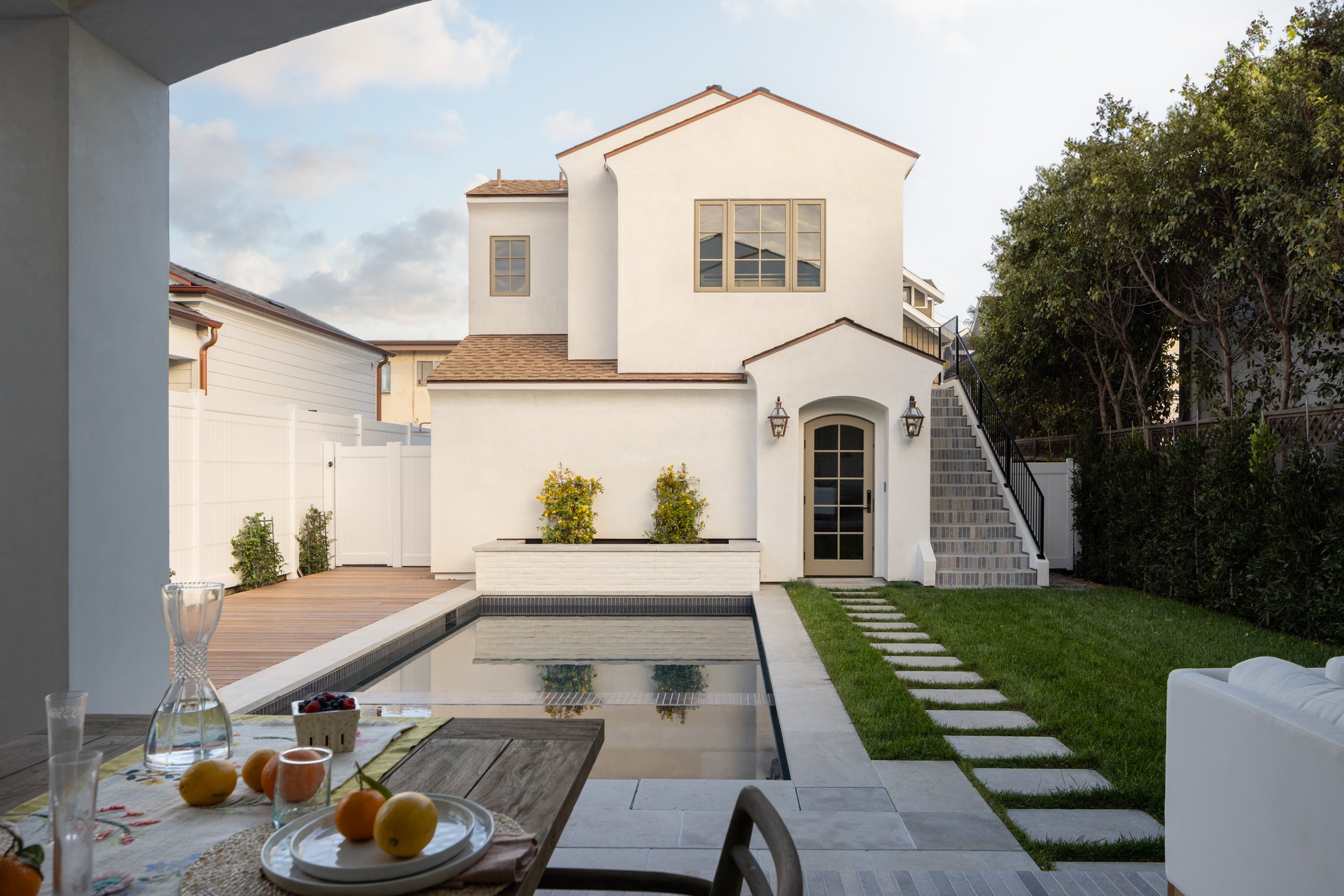 Contemporary white house with backyard pool, outdoor dining, and lush greenery.