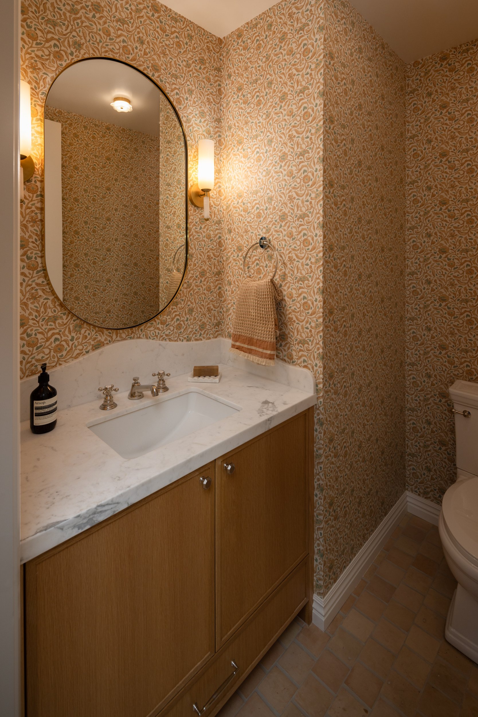 Bathroom vanity with marble countertop and vintage wallpaper.