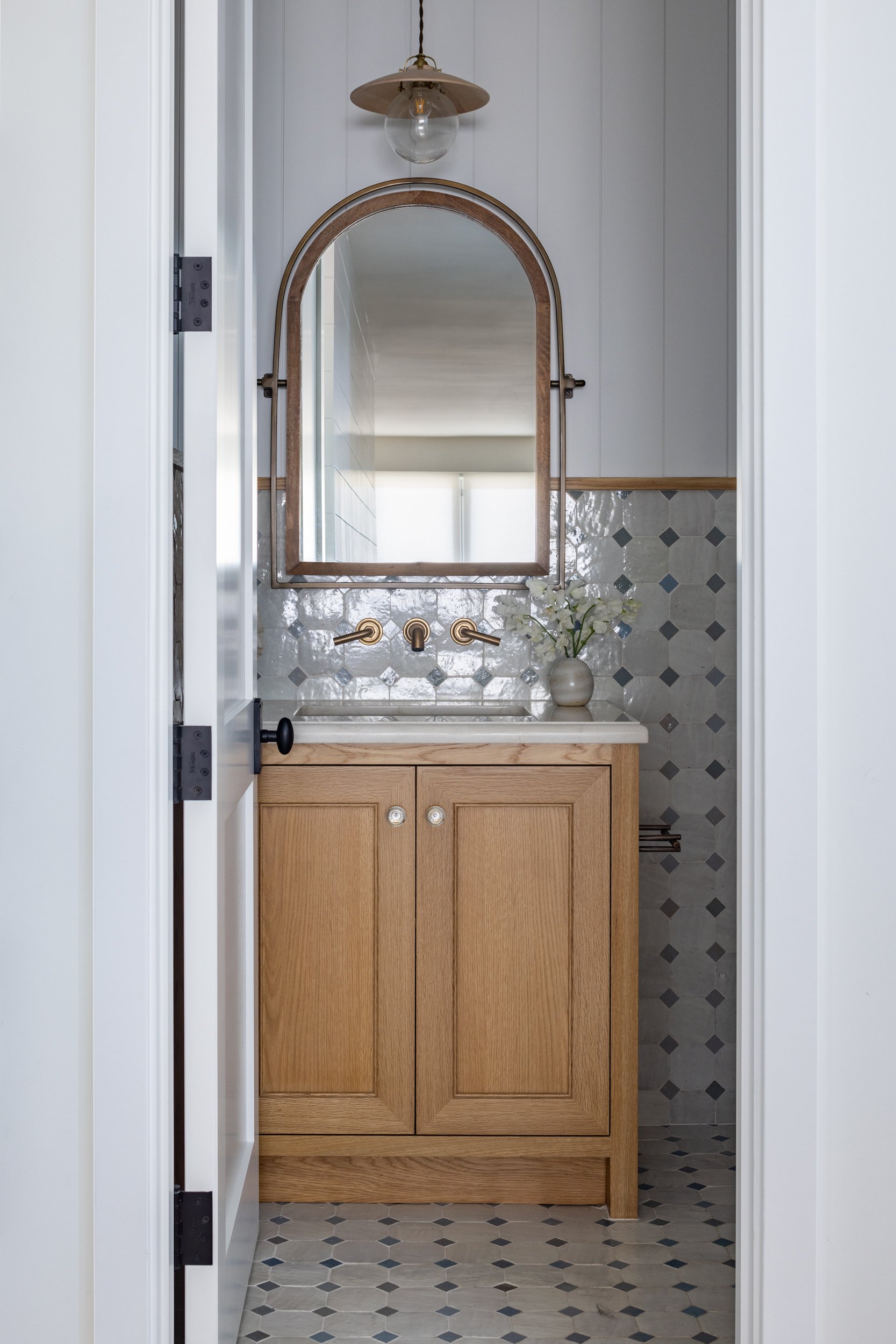 Bathroom vanity with wooden cabinet and elegant arched mirror design.