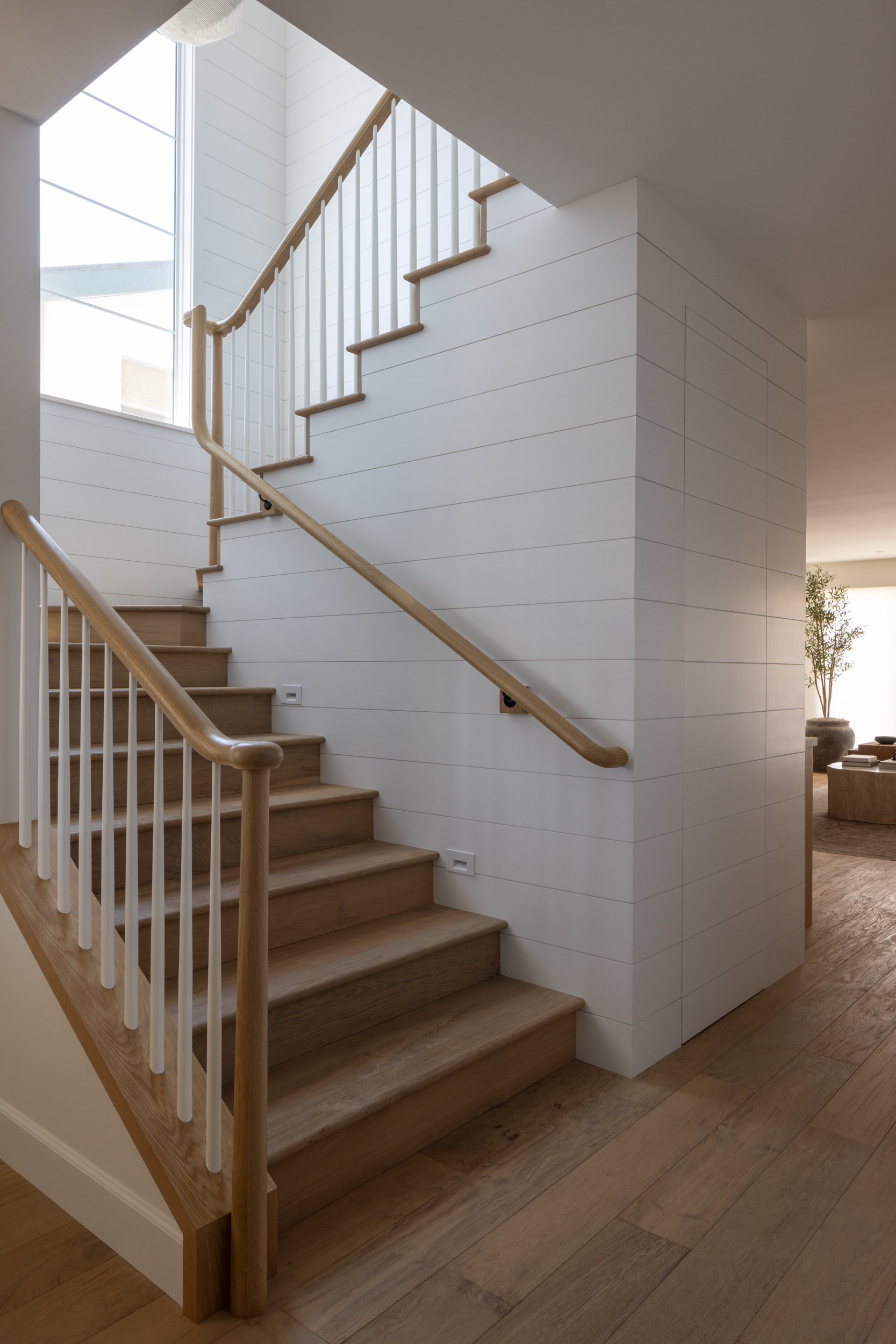 Elegant wooden staircase with white wall paneling, perfect for contemporary interior design.