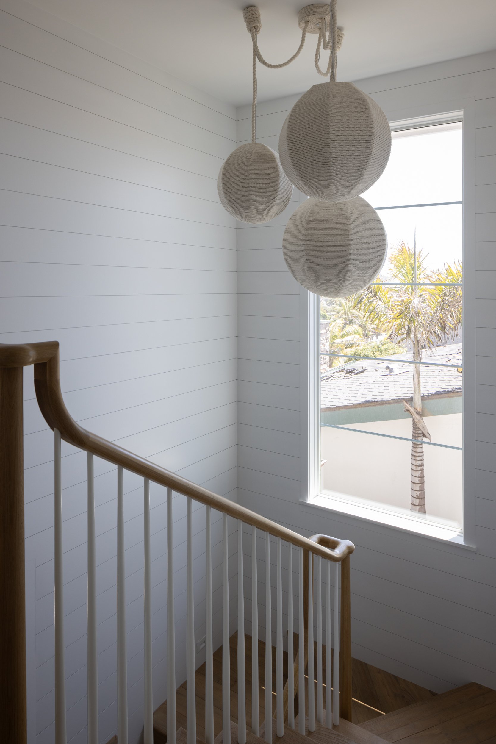 Contemporary spherical pendant lights in a bright coastal-style stairwell.