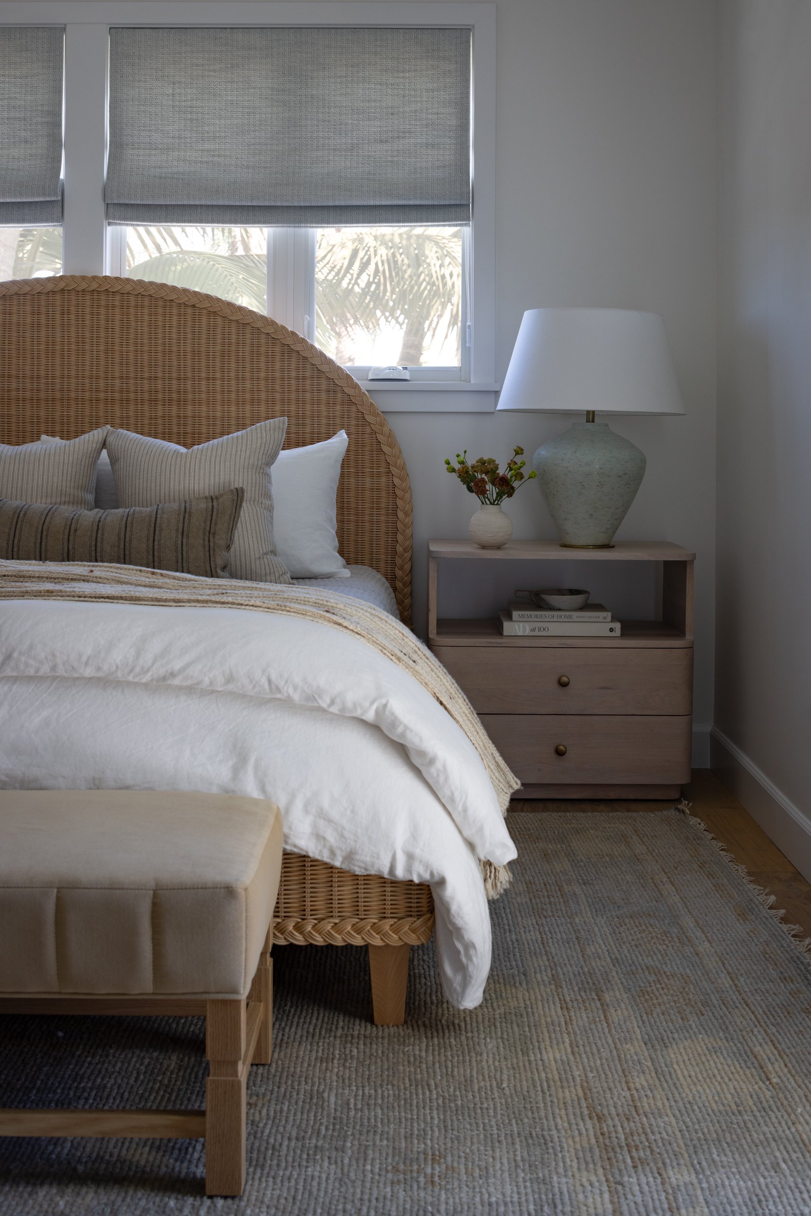 Cozy bedroom featuring a rattan headboard, neutral bedding, and natural light from large windows.