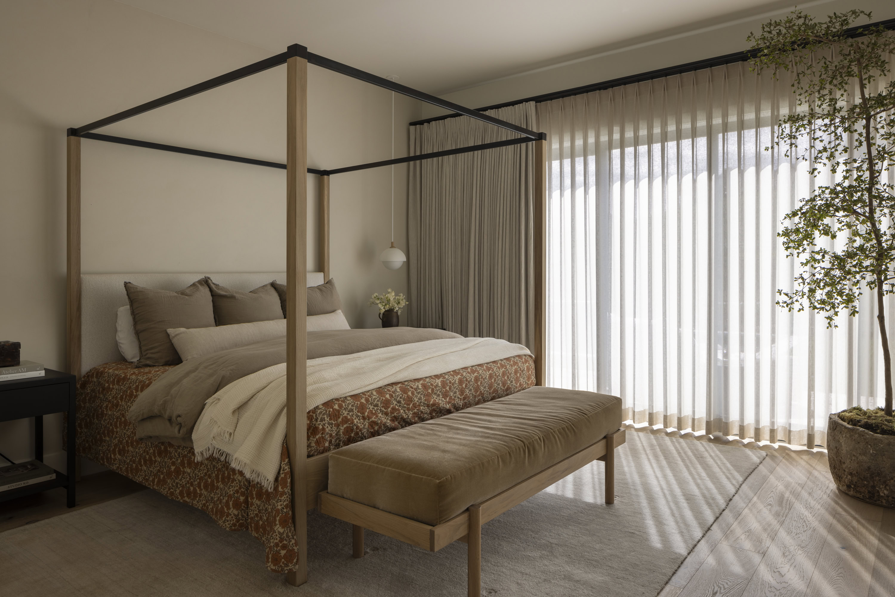 Canopy bed in a stylish bedroom with large windows and sheer curtains, creating a bright and airy at.