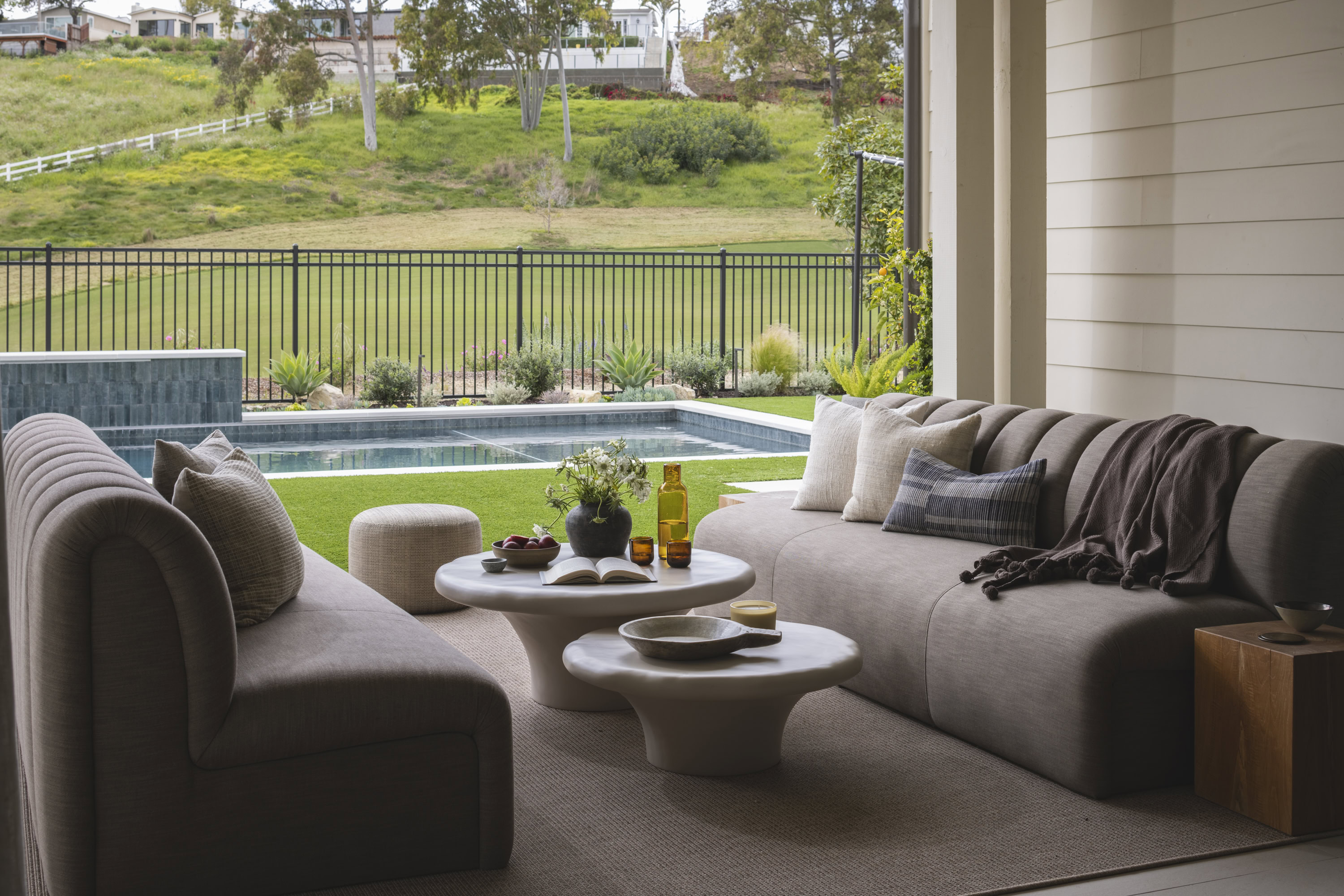 Elegant living room interior with comfortable sofas overlooking a lush backyard and pool area. Perfe.