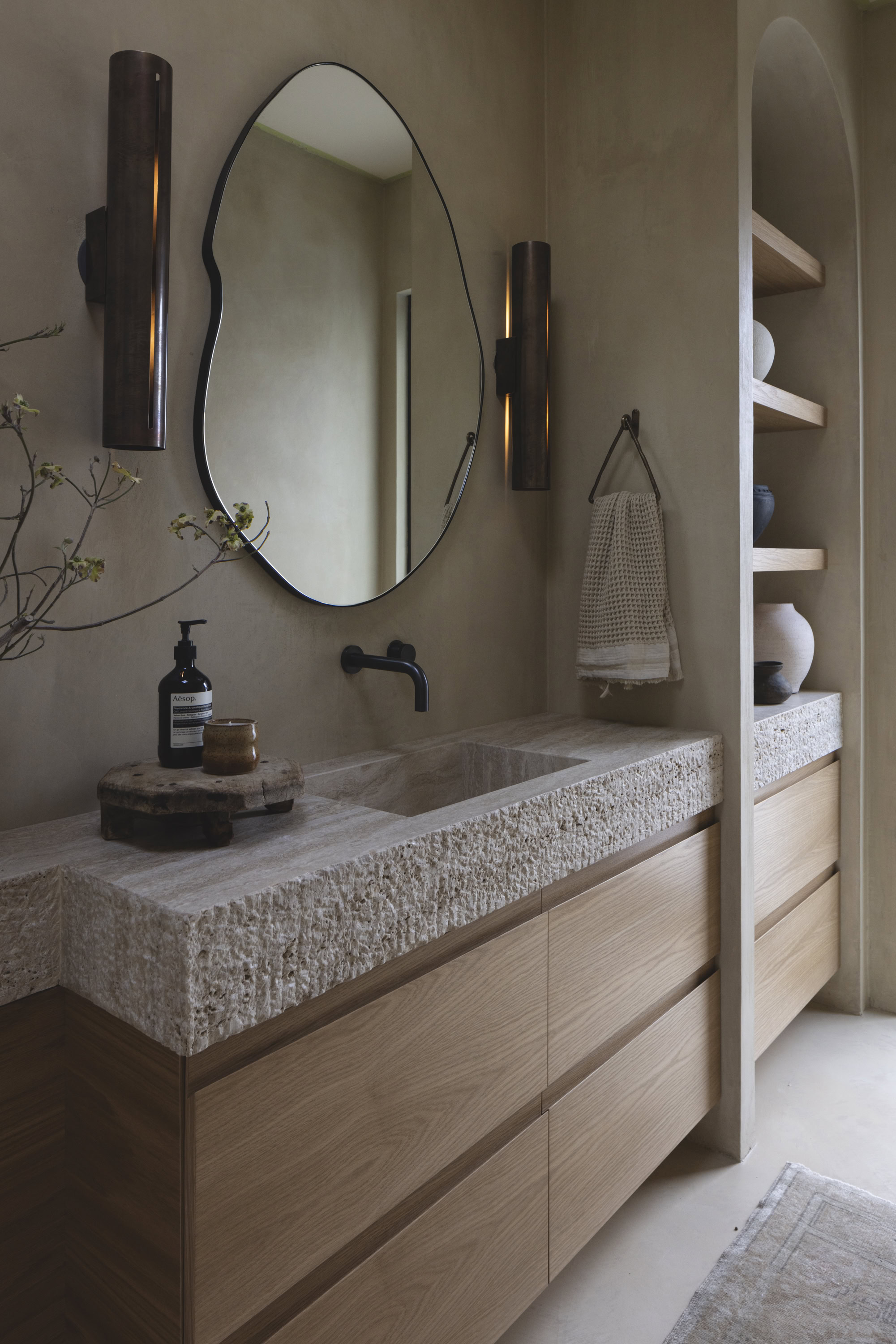 Elegant bathroom vanity featuring textured stone surface, oval mirror, and contemporary lighting fix.