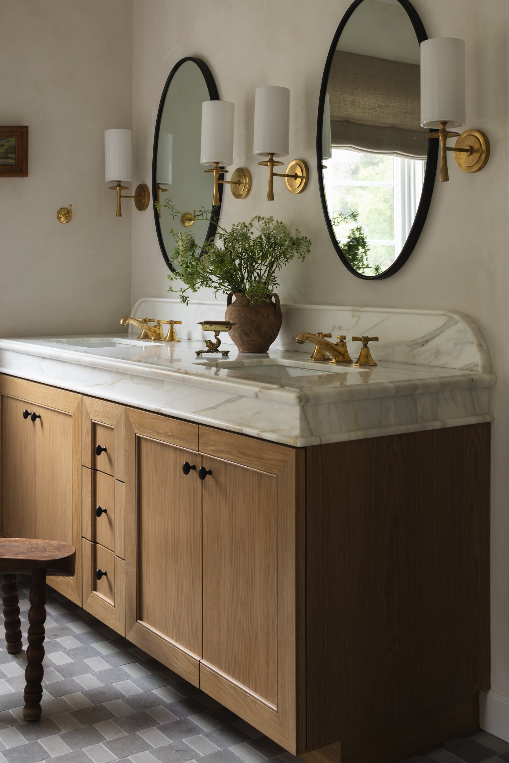 Elegant bathroom vanity with marble countertop and round mirrors, featuring gold fixtures.
