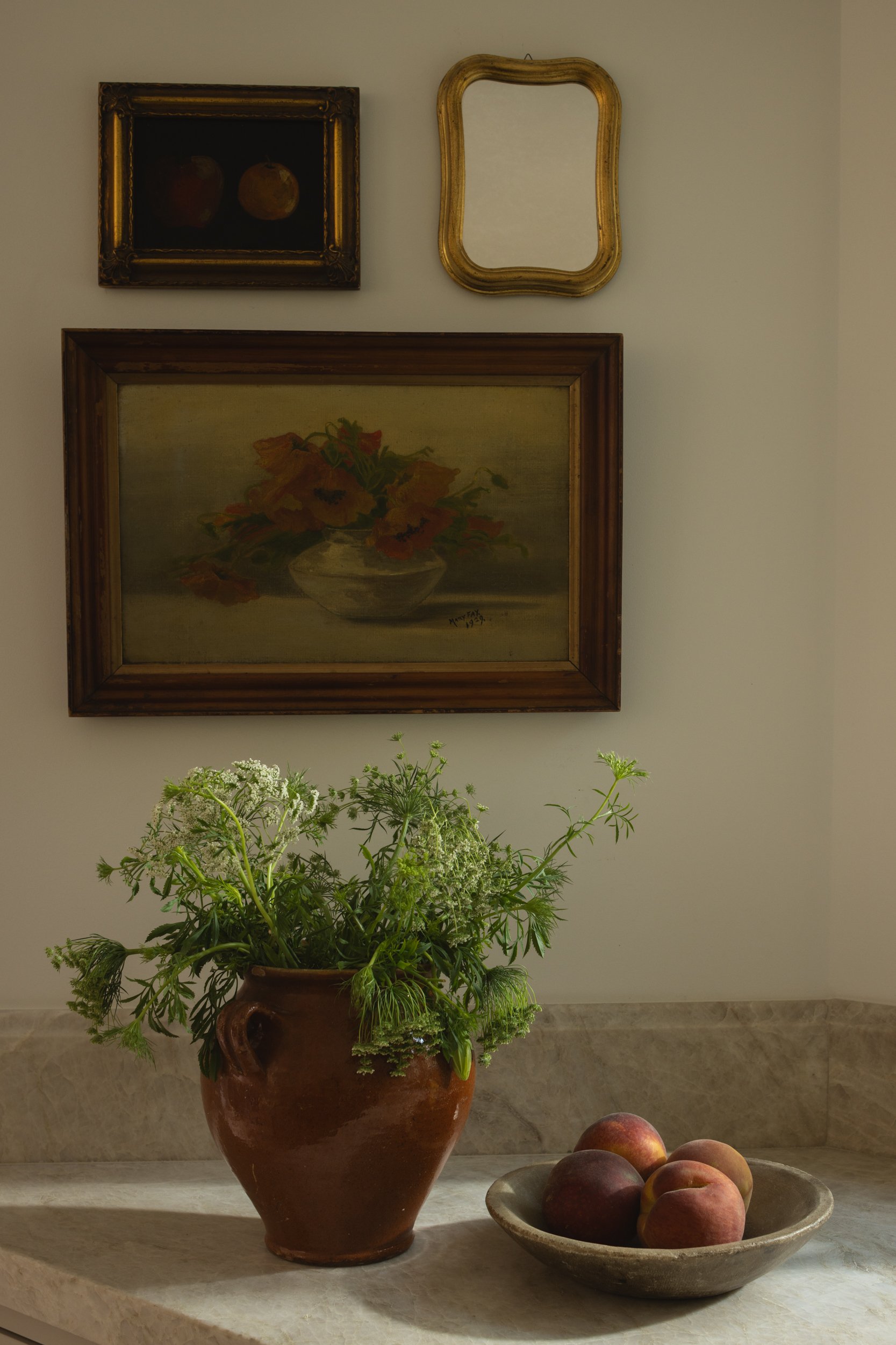 Vintage art and empty frames adorn a neutral wall in a stylish interior setting.