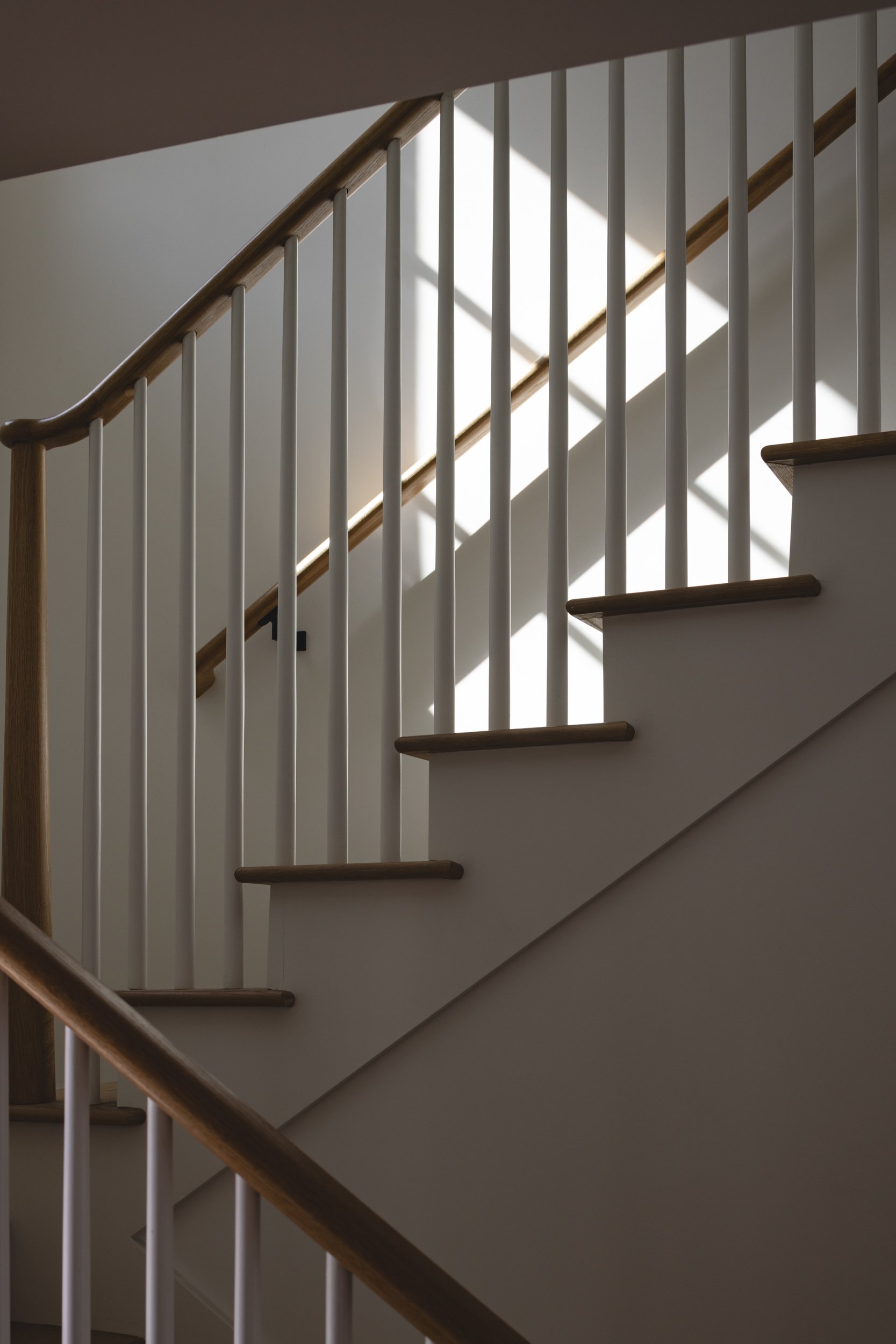Staircase featuring white balusters and wooden handrail illuminated by sunlight, showcasing contempo.