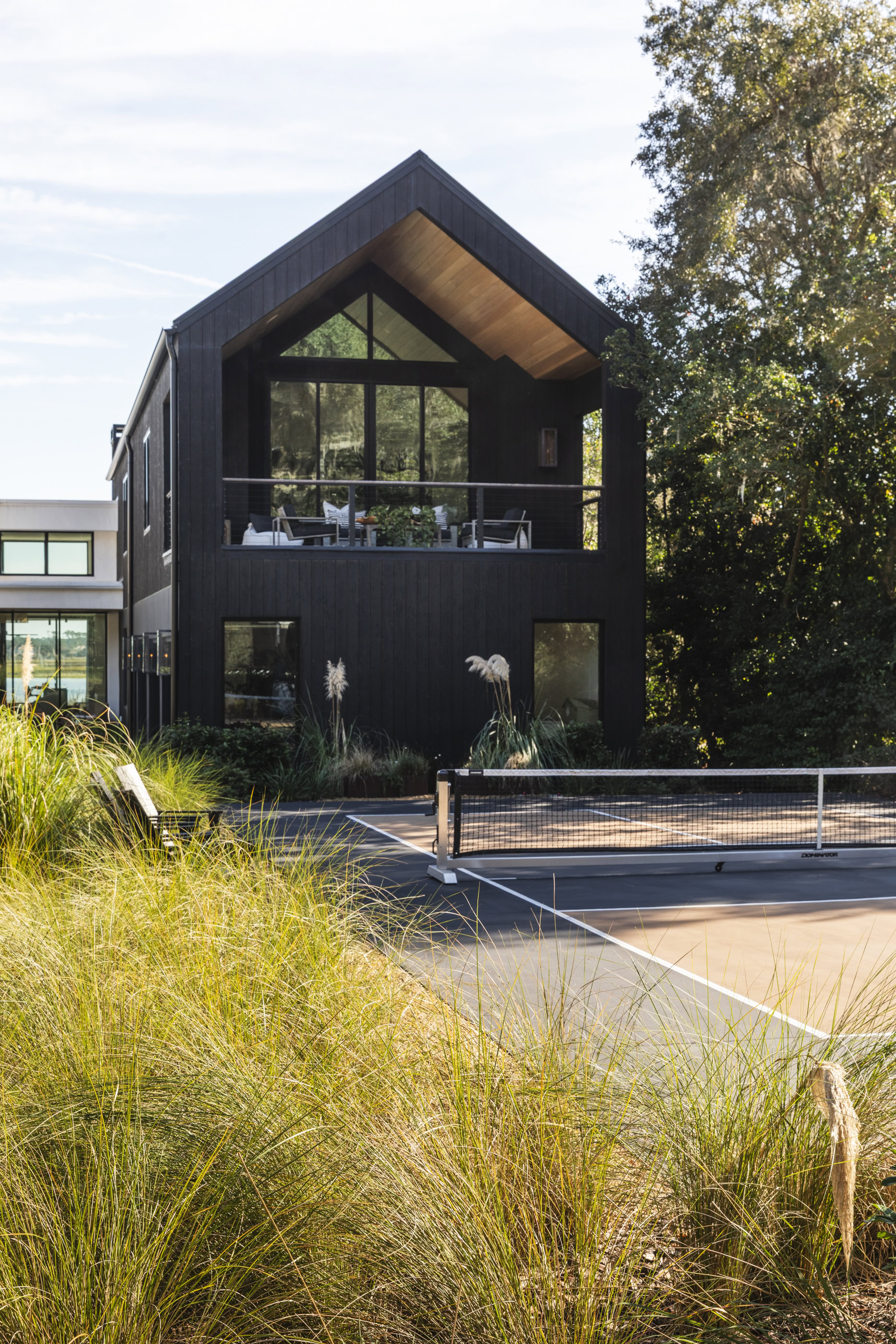 Modern black house with large glass windows and a balcony, surrounded by lush greenery and outdoor l.