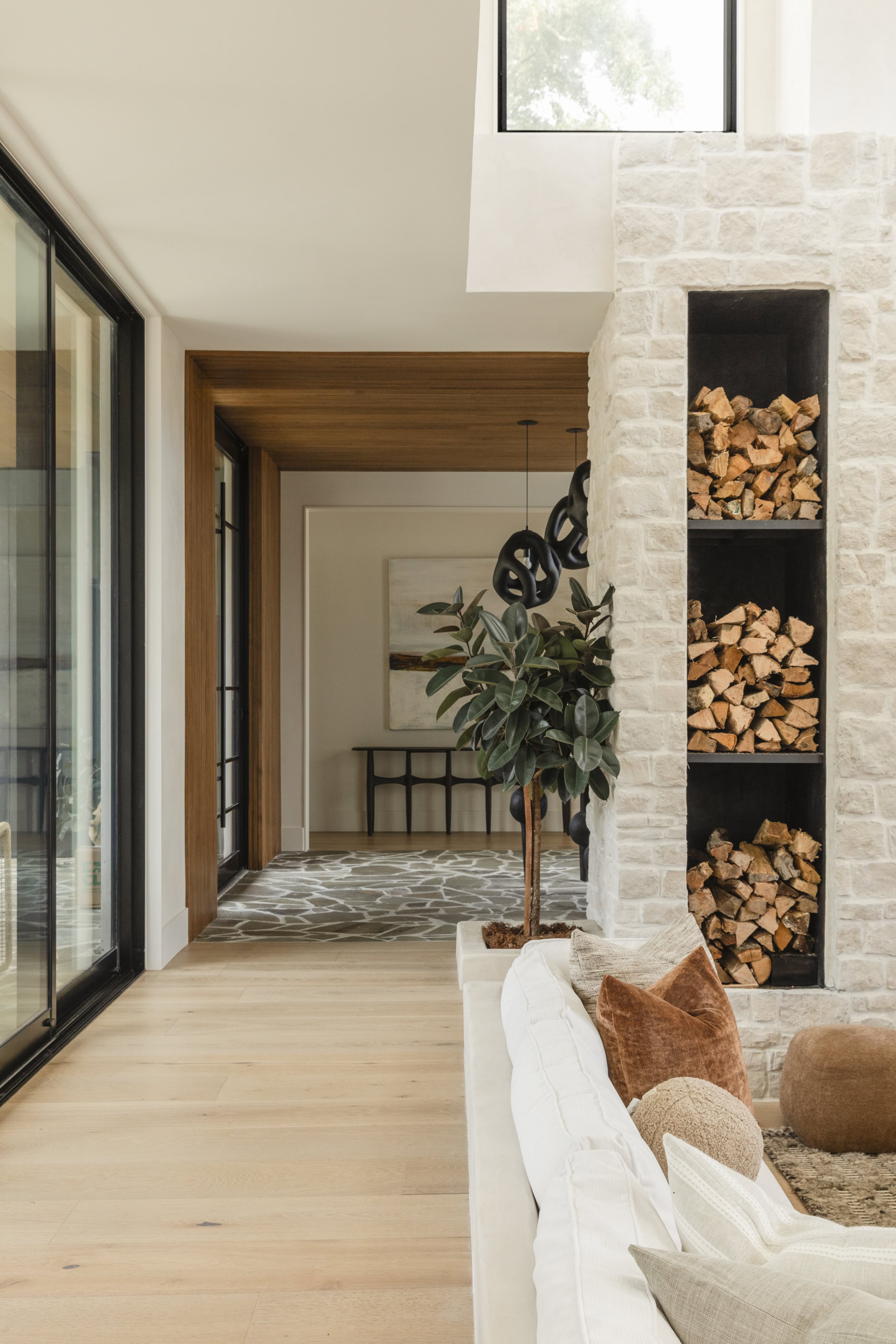 Contemporary living room featuring a wood storage fireplace, large windows, and stylish decor. Brigh.