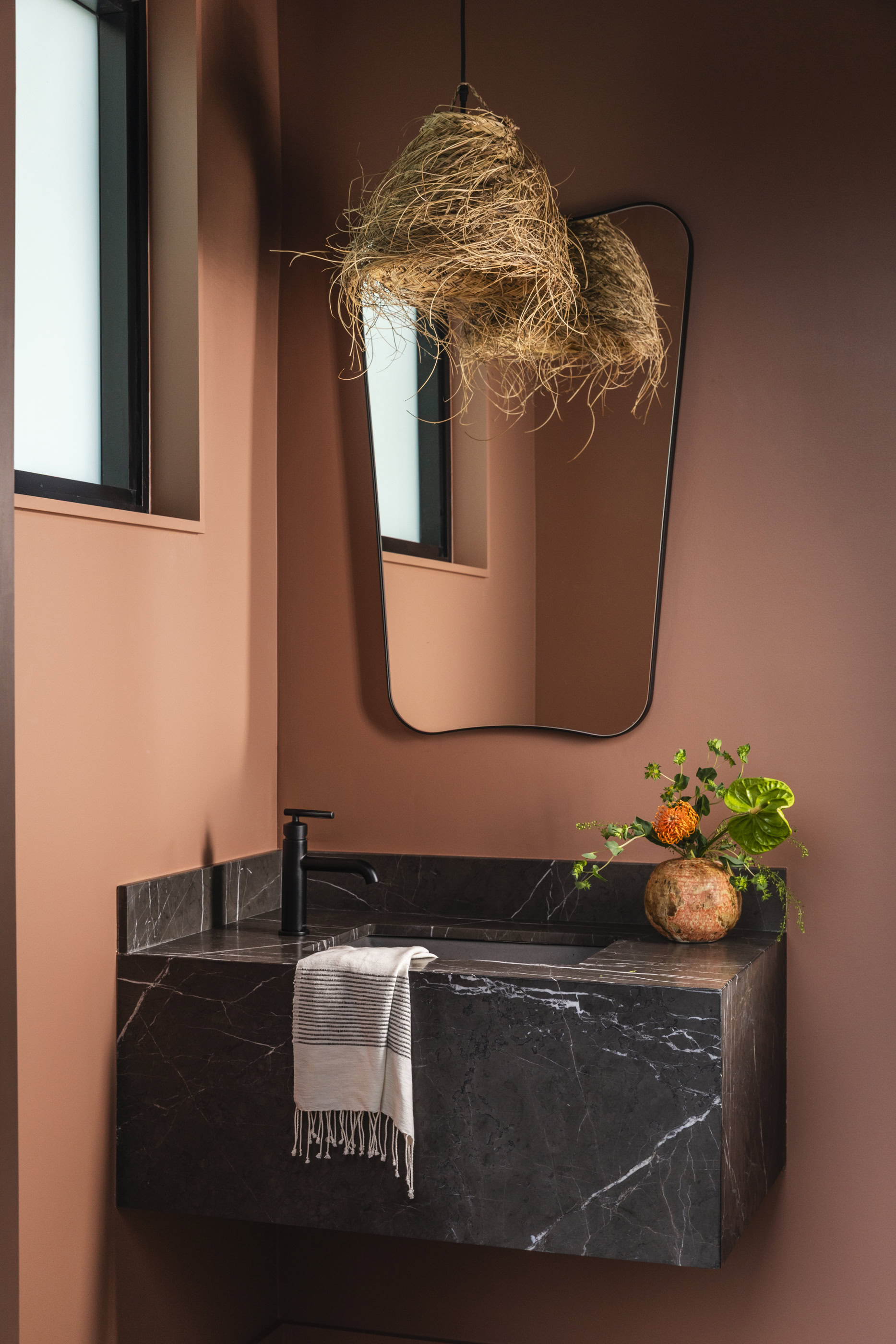 Modern bathroom vanity with black marble countertop and unique hanging light fixture.