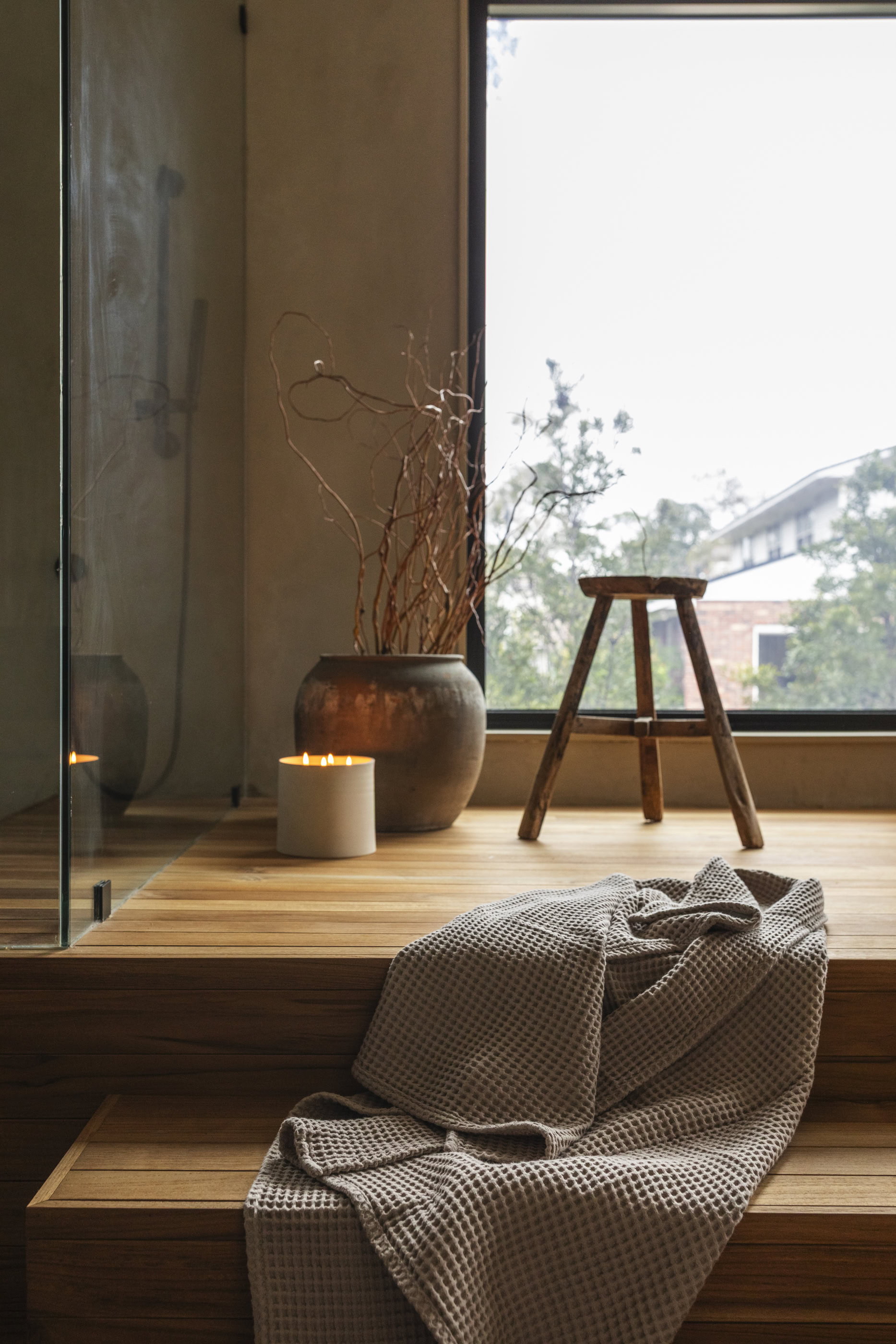 Elegant interior featuring a wooden platform, decorative vase, and cozy blanket near a large window.