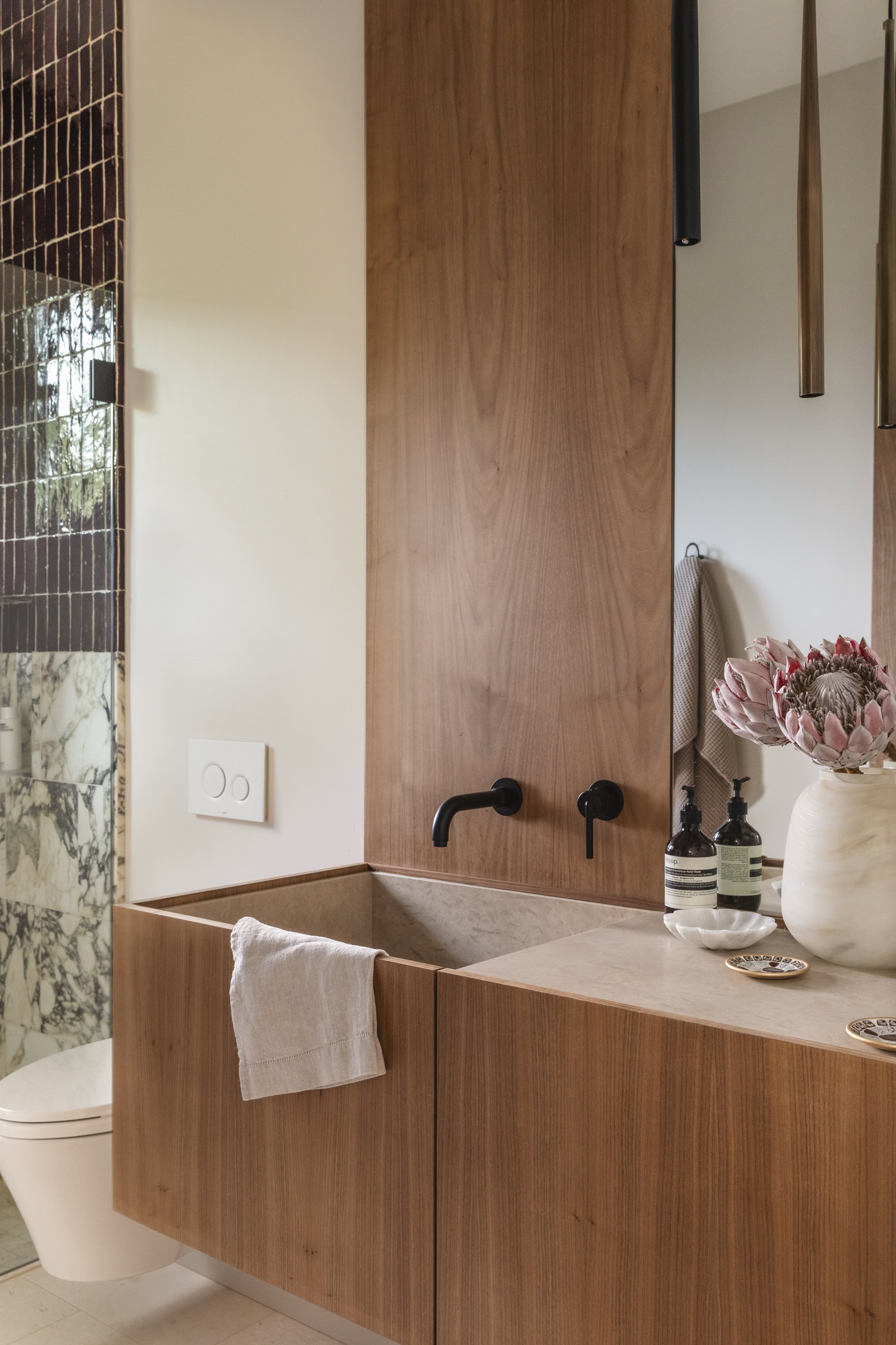 Elegant wooden bathroom vanity featuring black wall-mounted faucets and a beige basin.