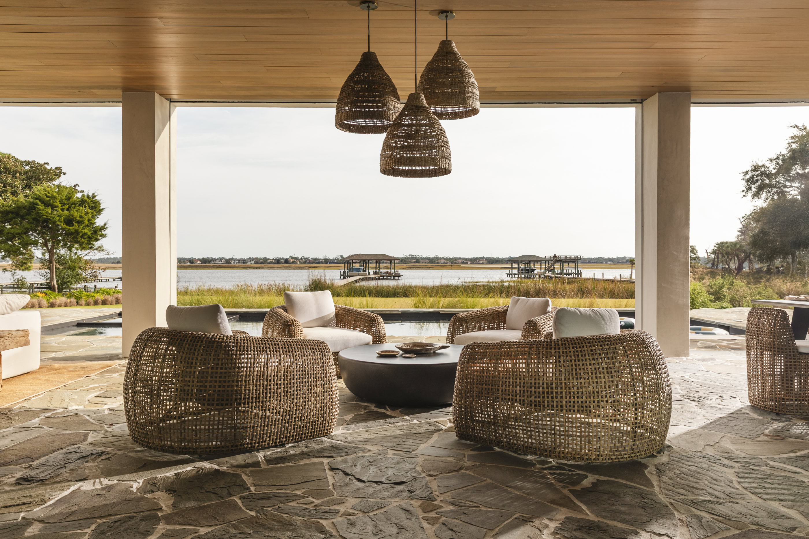 Outdoor lounge with wicker chairs and hanging pendant lights overlooking water.