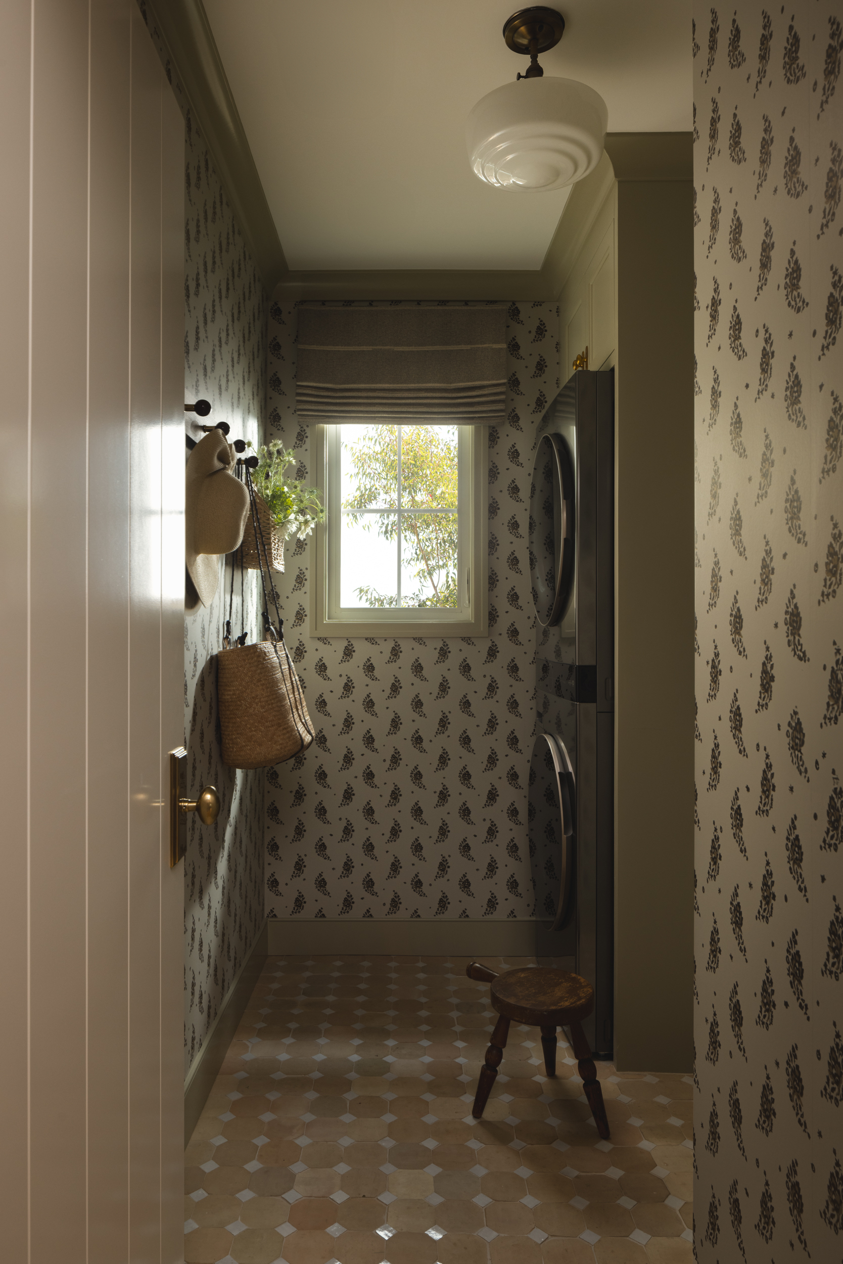 Cozy laundry room with patterned wallpaper, window, and stacked washer and dryer.
