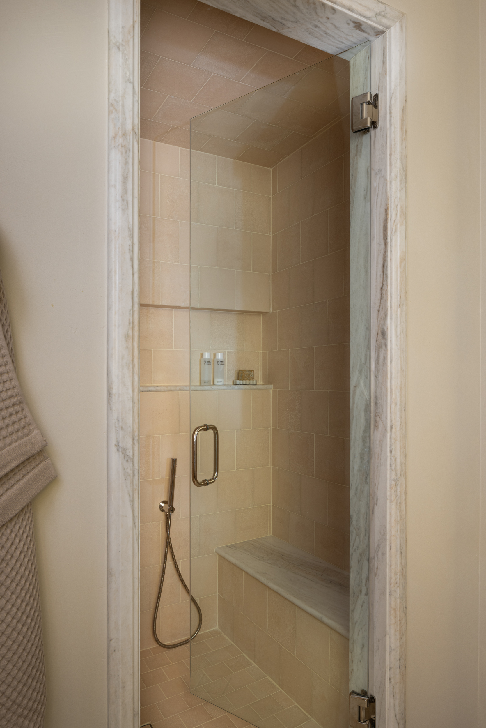 Modern walk-in shower with beige tiles and glass door at South Harlow Interiors.