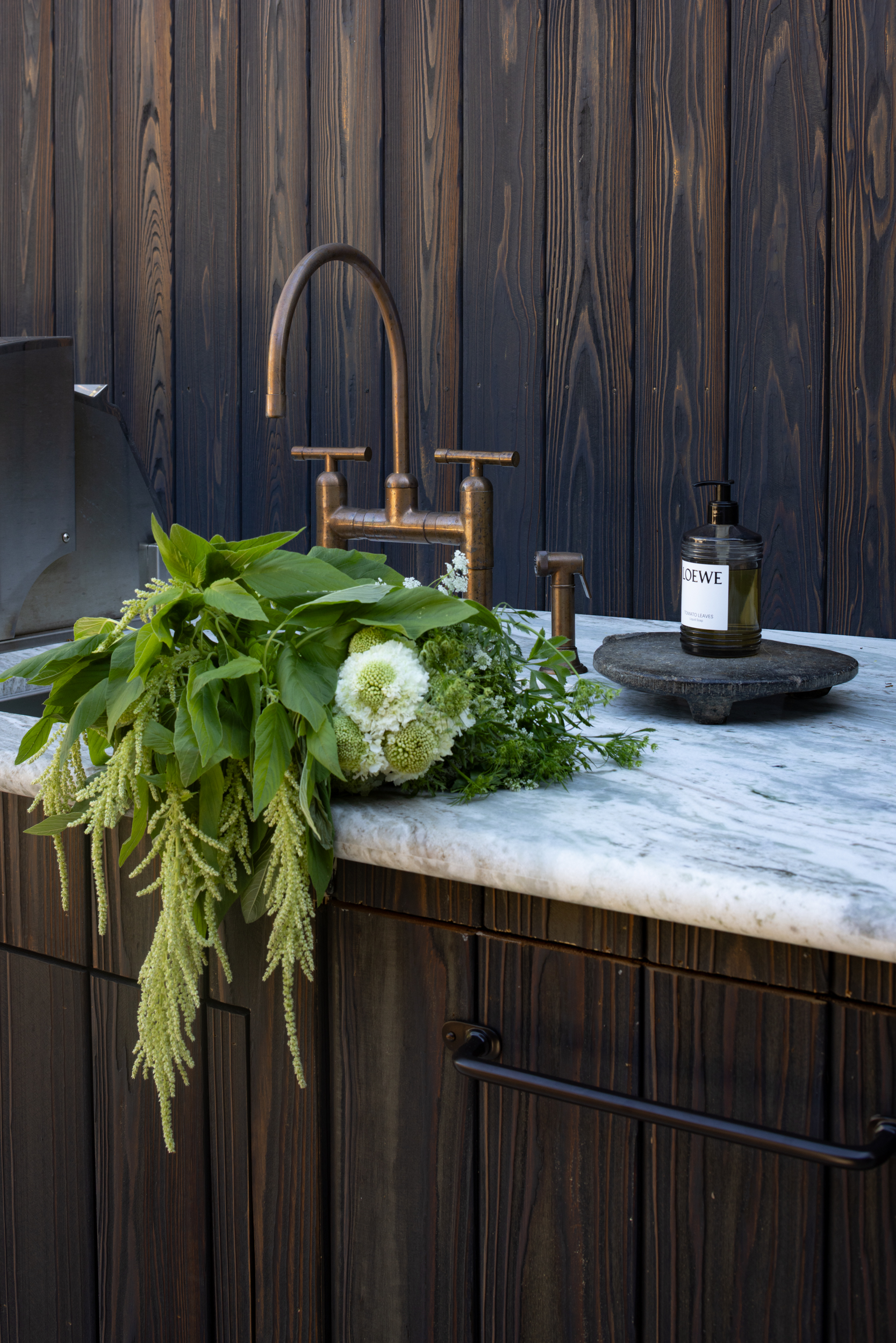 Modern kitchen with dark wood cabinets, marble countertop, and greenery decor.
